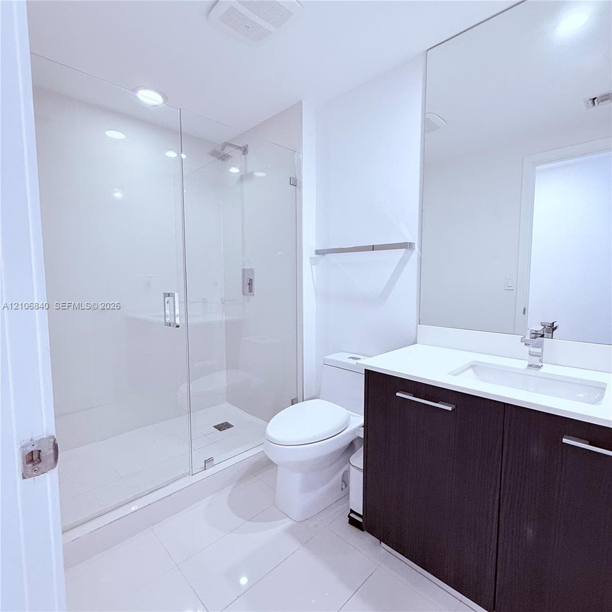 Bathroom featuring a glass-enclosed walk-in shower, dark-toned vanity with a light-colored countertop, integrated rectangular sink, and floor-to-ceiling mirror