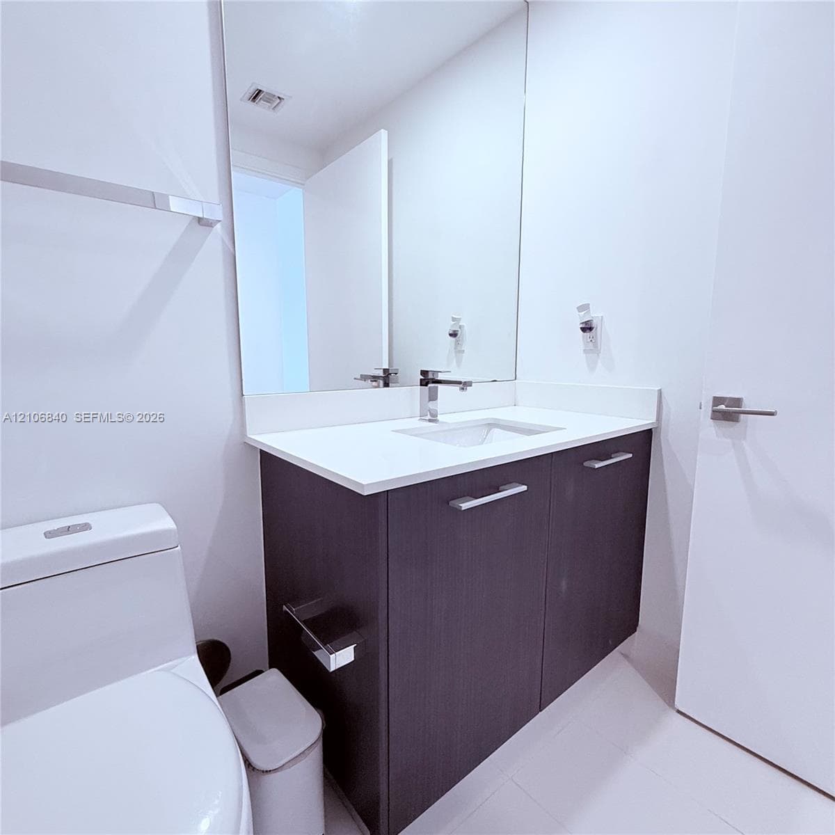 Bathroom featuring a dark wood-finish vanity, solid white countertop with an integrated basin, chrome-finish faucet, and full-height wall mirror