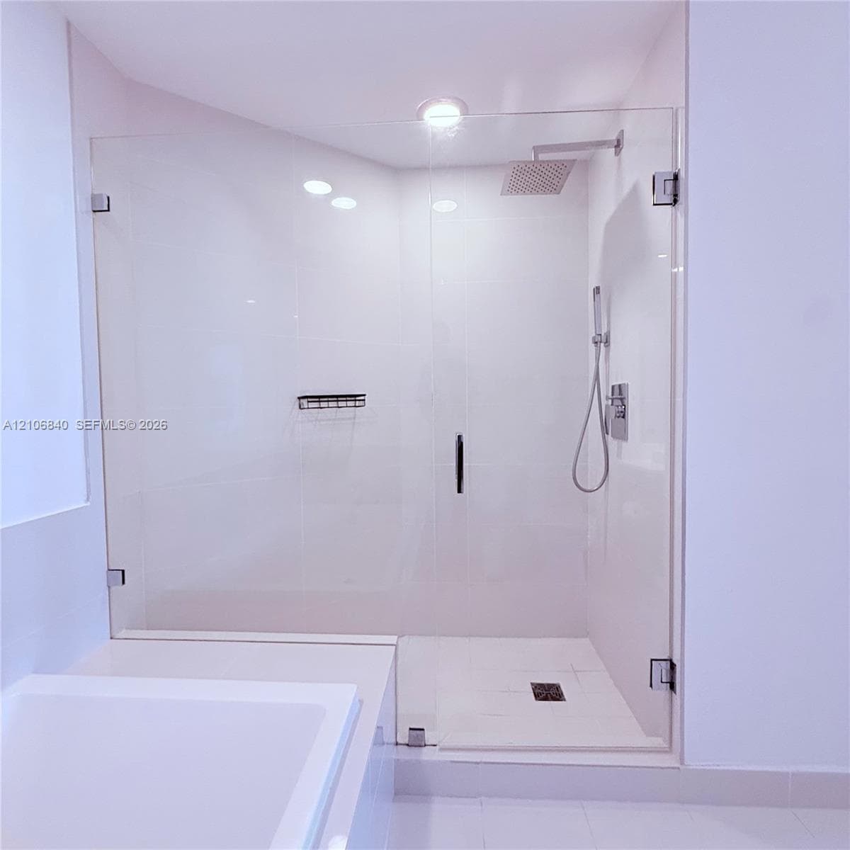 Walk-in shower featuring a frameless glass enclosure, rainfall showerhead, handheld shower attachment, integrated wall niche, and tile flooring