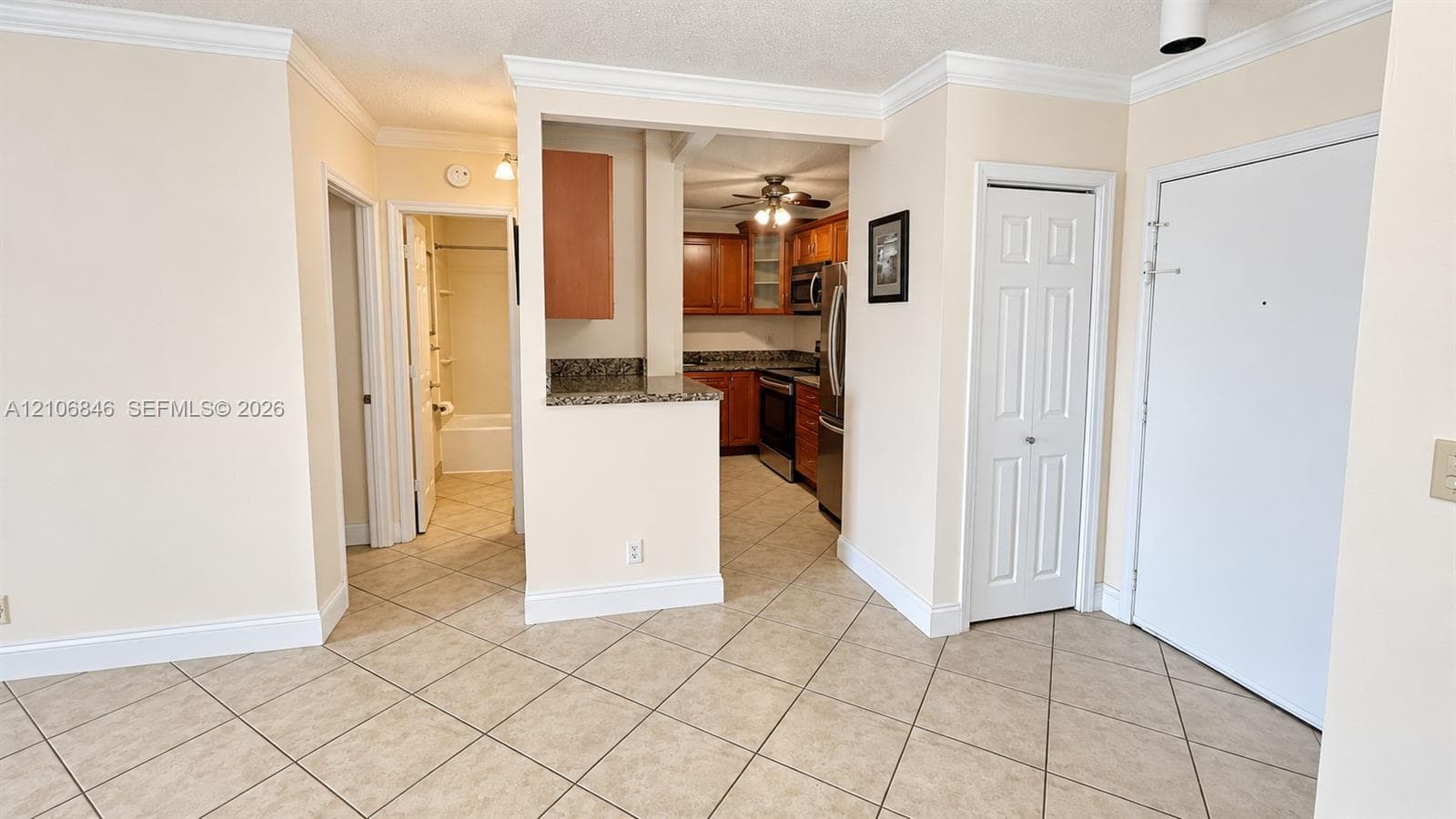 Interior space featuring diagonal ceramic tile flooring, crown molding, a kitchen with stone countertops and wood-finish cabinetry, and a bi-fold door closet