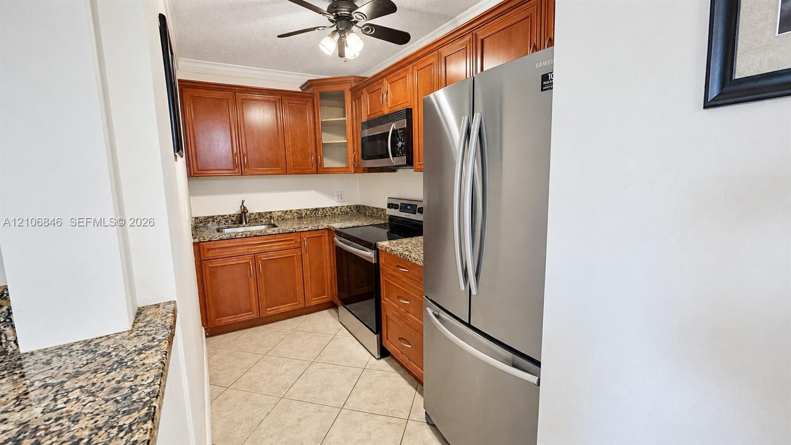 Kitchen featuring stained wood cabinetry, stone-surface countertops, tile flooring, and stainless steel appliances including a built-in microwave and refrigerator