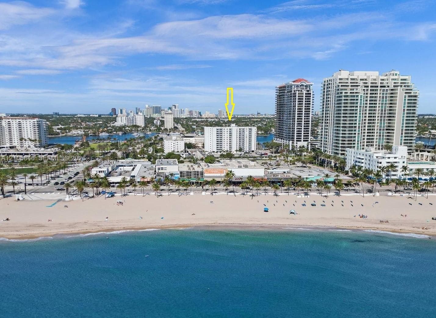 Aerial perspective of a high-rise residential structure positioned on the coast, featuring direct proximity to the shoreline, sand beach, and maritime surroundings