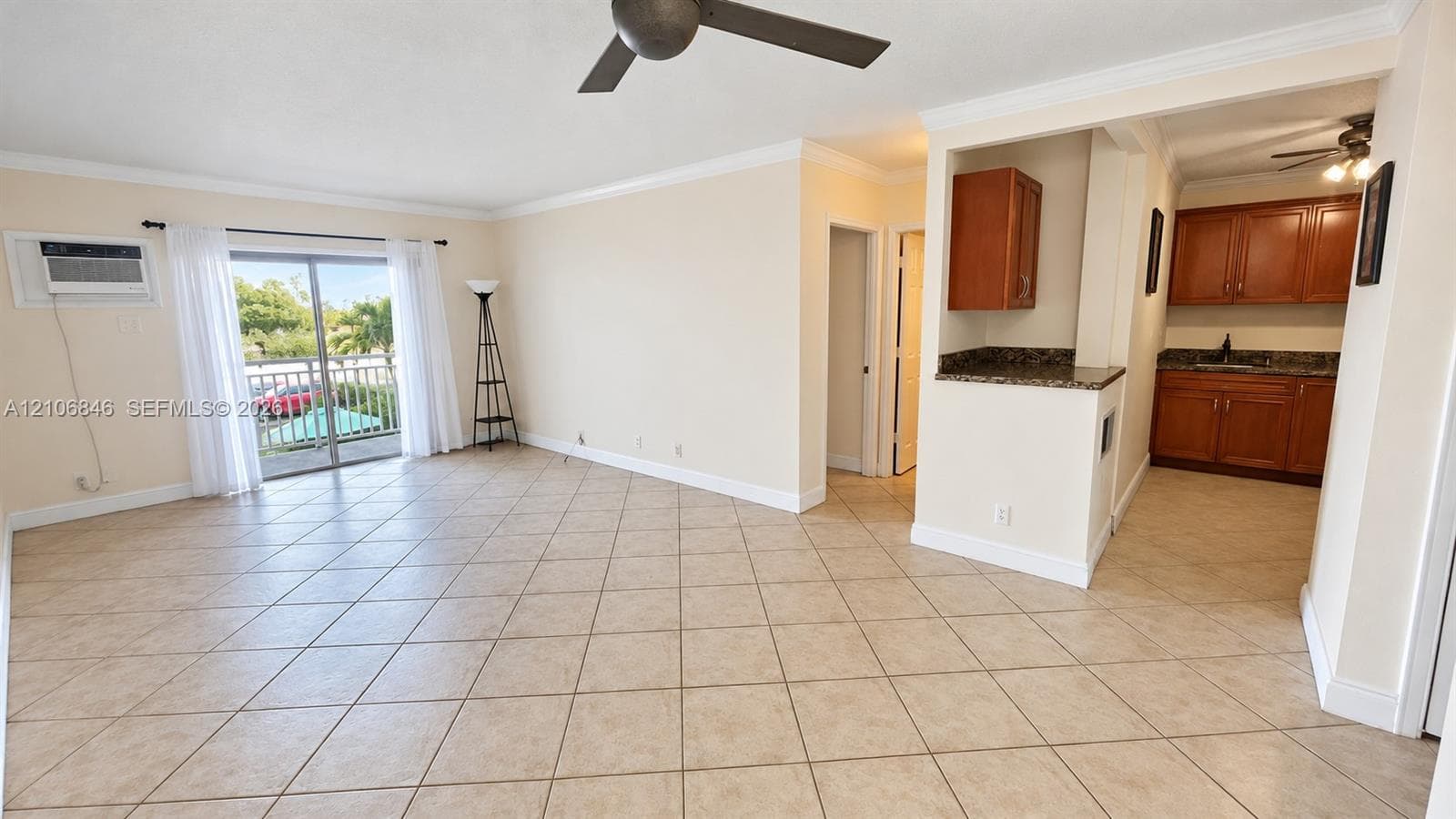 Open floor plan featuring diagonal ceramic tile flooring, sliding glass doors to a private balcony, crown molding, and wooden cabinetry