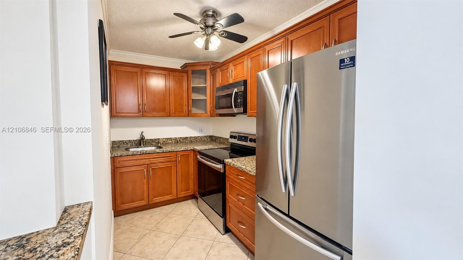 Kitchen featuring medium-toned wood cabinetry, stone-finish countertops, stainless steel appliances, ceramic tile flooring, and a ceiling-mounted light fixture