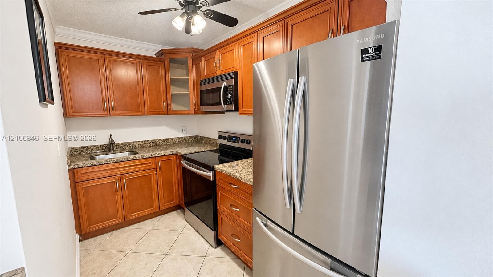 Kitchen featuring natural-finish wood cabinetry, stone-patterned countertops, stainless steel appliances, tile flooring, and a ceiling fan