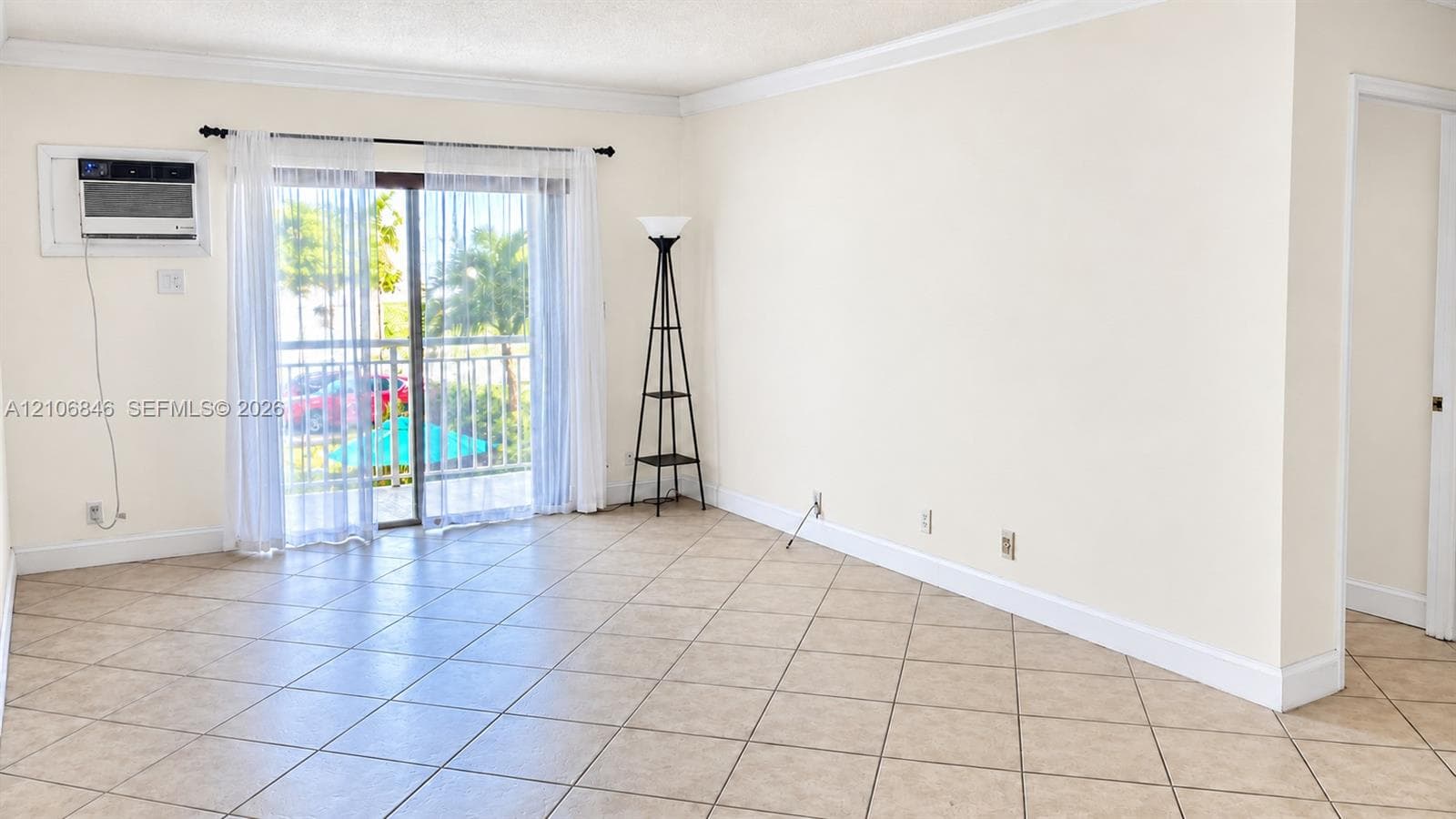 Neutral-toned interior featuring ceramic tile flooring, crown molding, and sliding glass doors with balcony access
