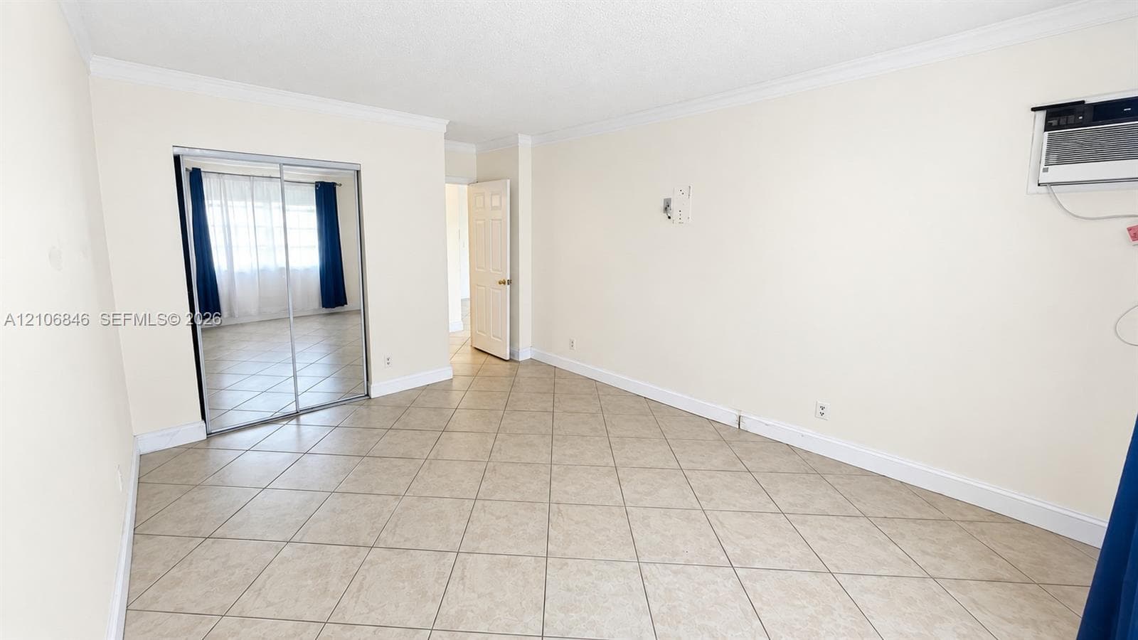 Interior room featuring neutral-toned tile flooring, crown molding, a sliding mirrored closet door, and a wall-mounted air conditioning unit