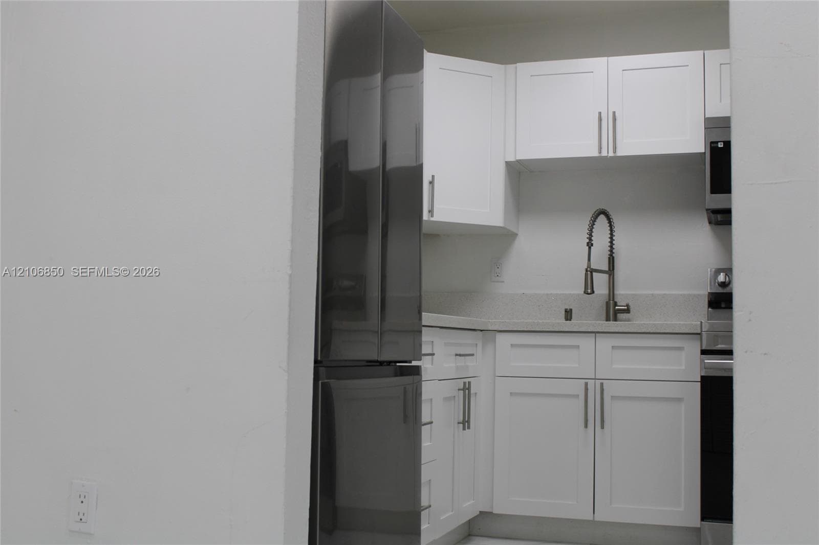 Kitchen featuring white shaker-style cabinetry, stainless steel refrigerator, stone-composite countertop, undermount sink with gooseneck faucet, and stainless steel microwave