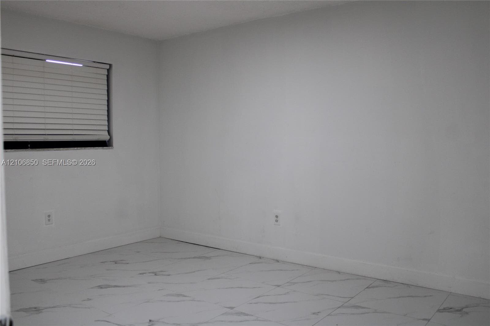 Neutral-toned interior space featuring light-colored tile flooring with a marble-finish pattern and a window equipped with horizontal blinds
