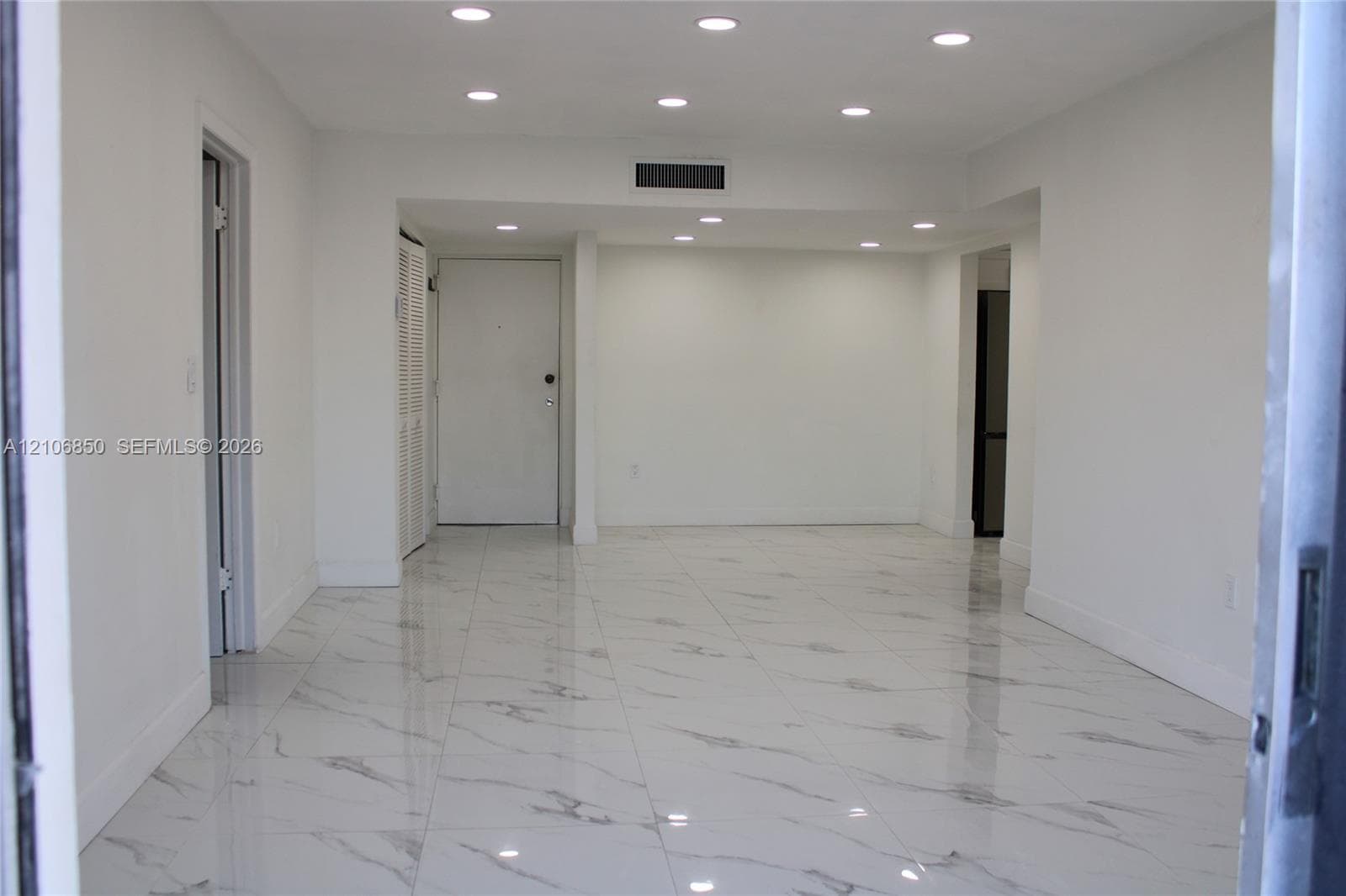 Interior space featuring high-gloss, large-format veined tile flooring, crisp white walls, and recessed ceiling lighting