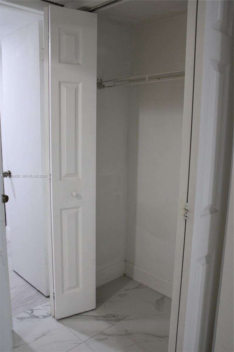 Storage closet featuring bi-fold panel doors and a built-in wire shelf, complemented by large-format stone-patterned tile flooring