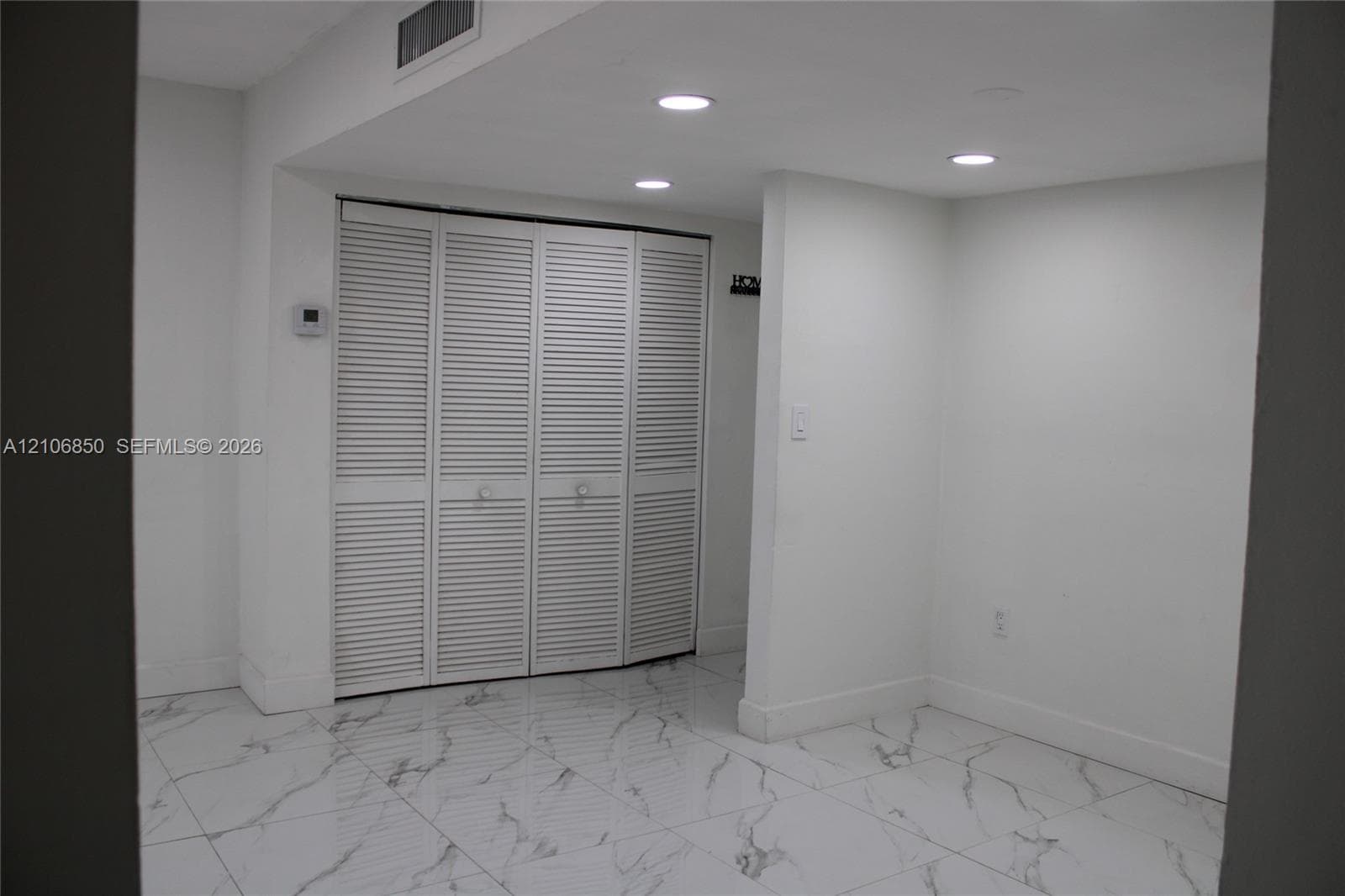 Interior space featuring white stone-finish flooring with grey veining, four-panel louvered closet doors, and recessed ceiling lighting