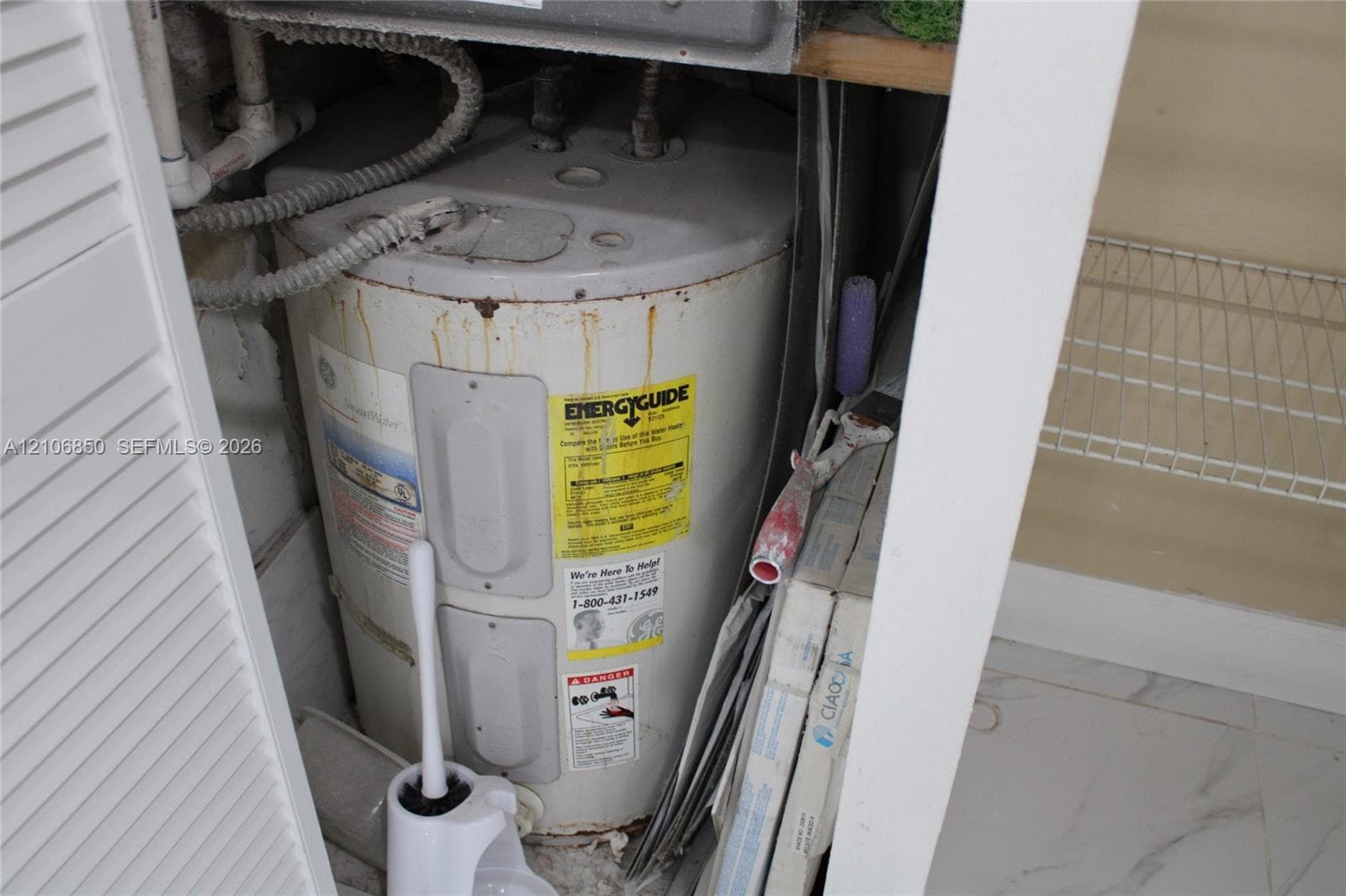Utility closet housing a water heater unit, featuring louvered door access and wire shelving