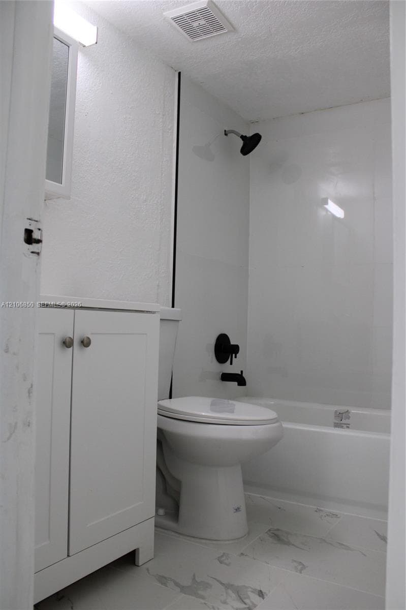 Bathroom featuring a white vanity cabinet, bathtub with a shower enclosure, and stone-finish tile flooring complemented by matte black plumbing fixtures