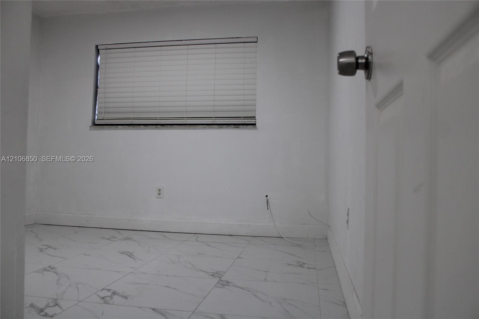 Room featuring white tile flooring with grey veining, neutral wall tones, and a window fitted with horizontal blinds
