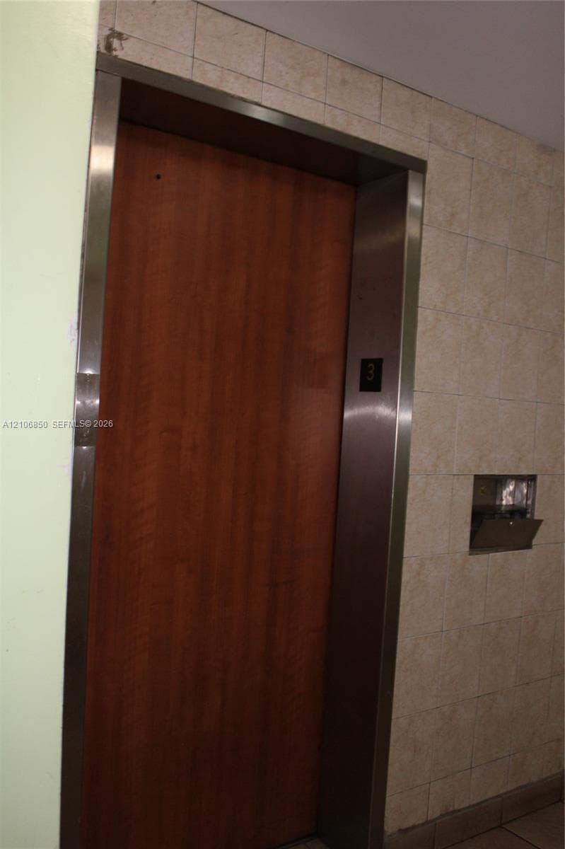 Elevator featuring a wood-finish door, stainless steel frame, and neutral-toned wall tiling