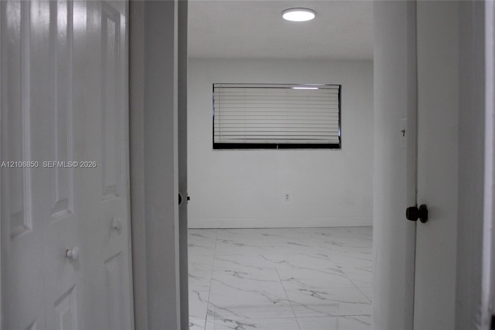Interior room featuring large-format light-toned tile flooring with veining, multi-panel closet doors, and a window with horizontal blinds