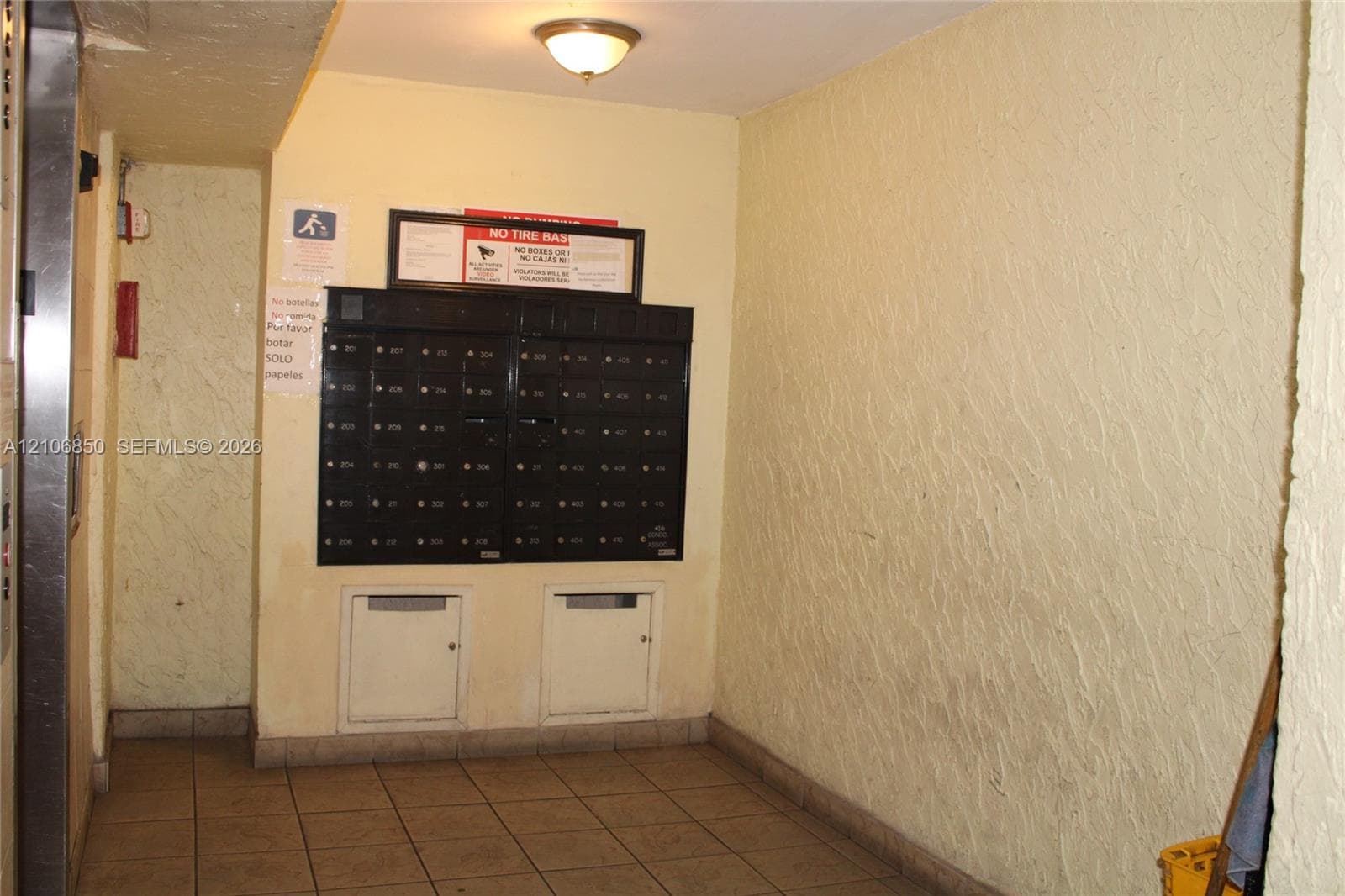 Common area mail center featuring a multi-unit black metal mailbox station, tiled flooring, and a ceiling-mounted light fixture