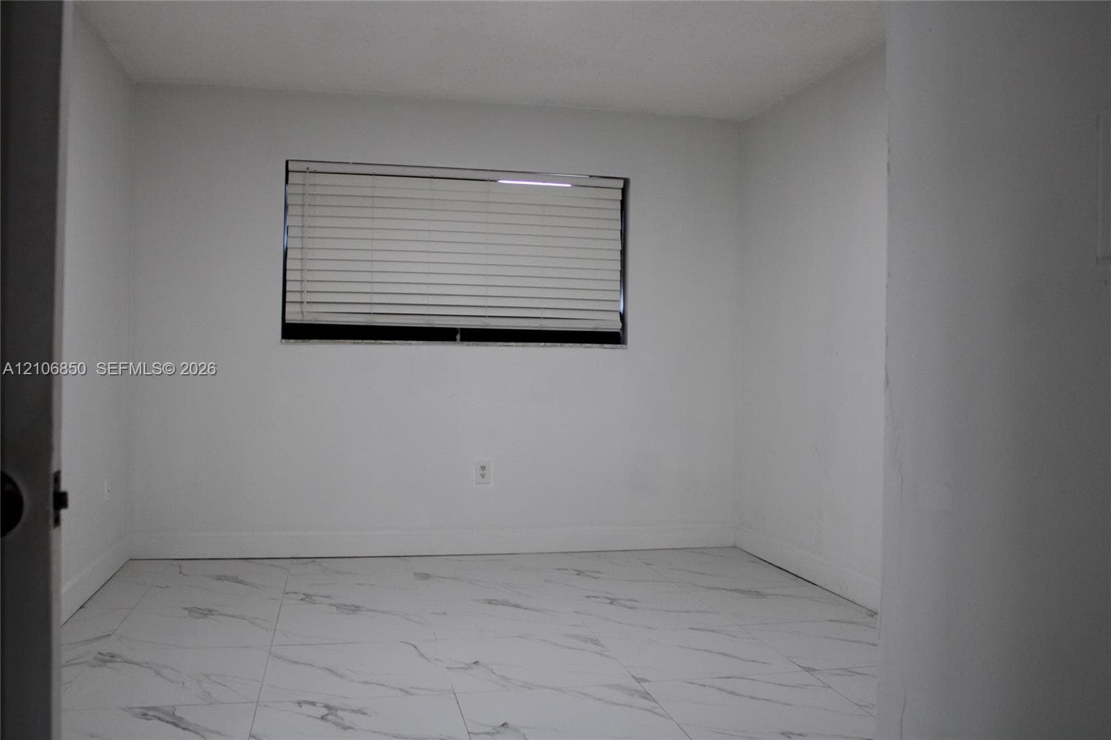 Interior room featuring large-format, white veined tile flooring, neutral wall finishes, and a window with horizontal blinds