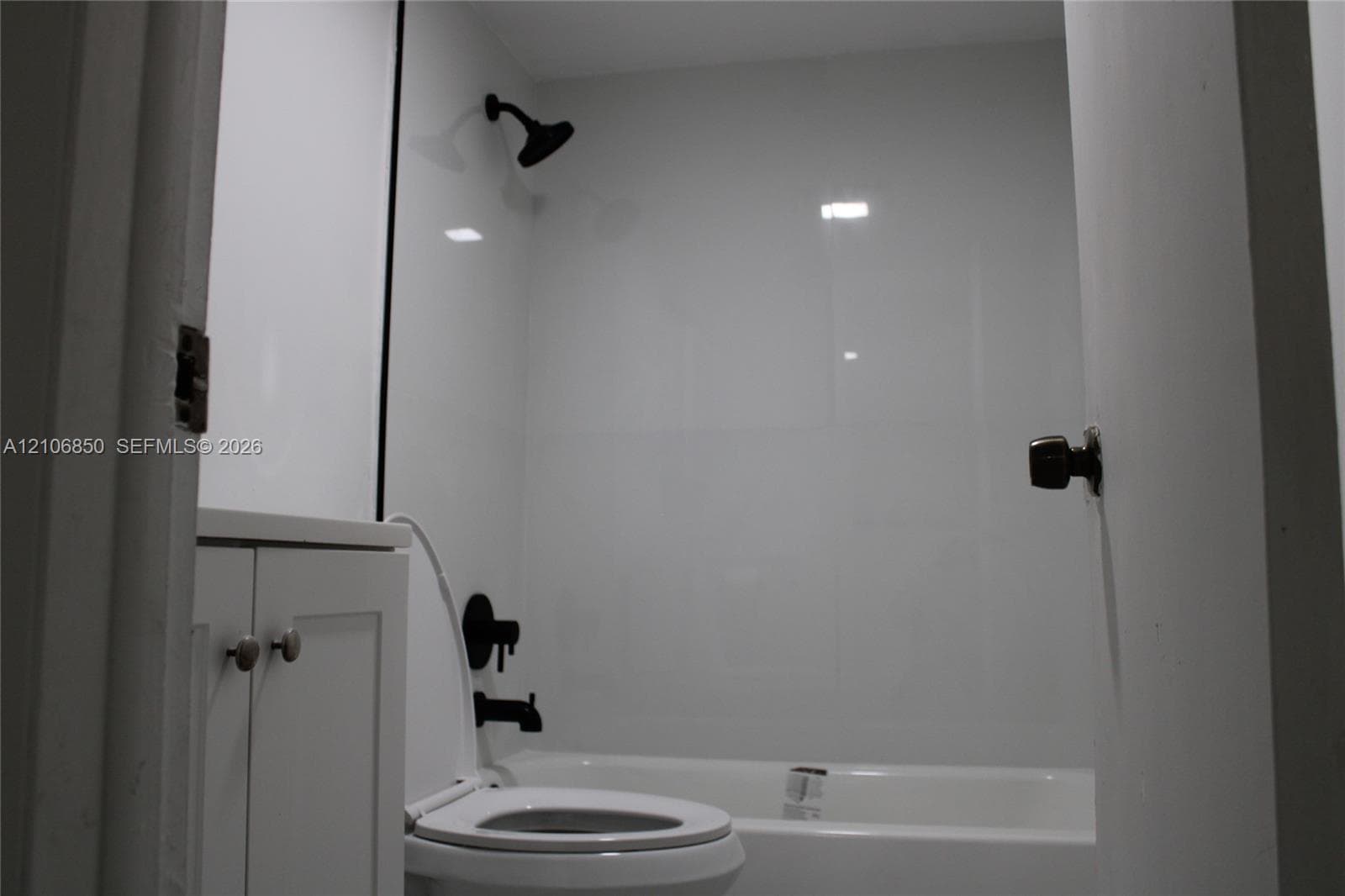 Bathroom featuring white panel shower surround, matte black showerhead and tub faucet, white vanity cabinet with circular pulls, and white standard toilet