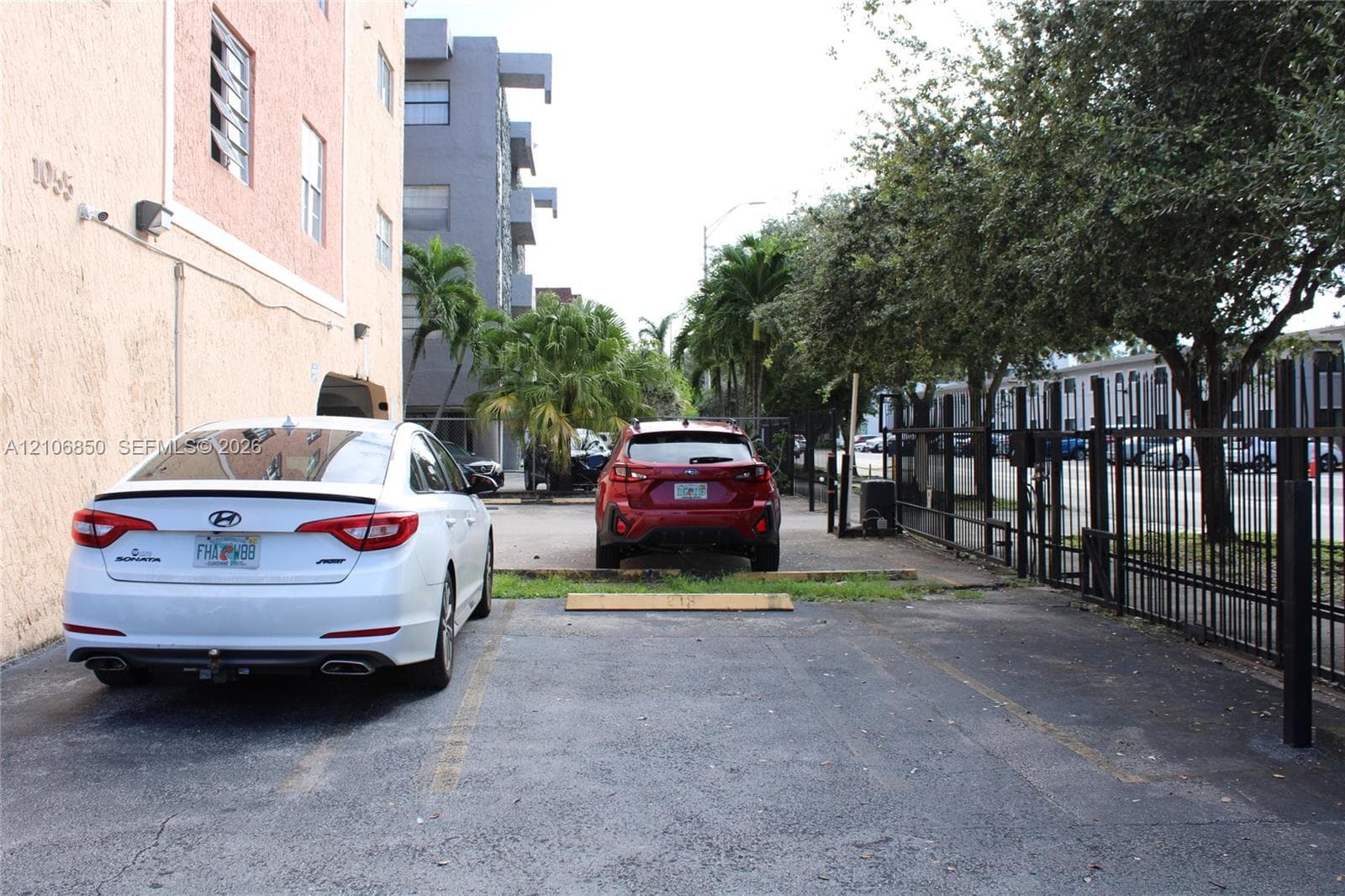 Dedicated asphalt parking area featuring metal perimeter fencing, concrete wheel stops, and mature landscaping