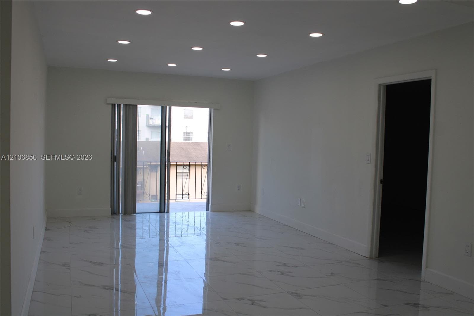 Interior space featuring high-gloss tile flooring with veining detail, recessed ceiling lighting, and sliding glass door access to an exterior balcony