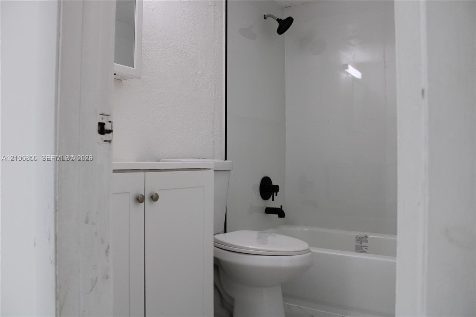 Bathroom featuring white shaker-style cabinetry, matte black hardware, wall-mounted shower head, and a white bathtub surround
