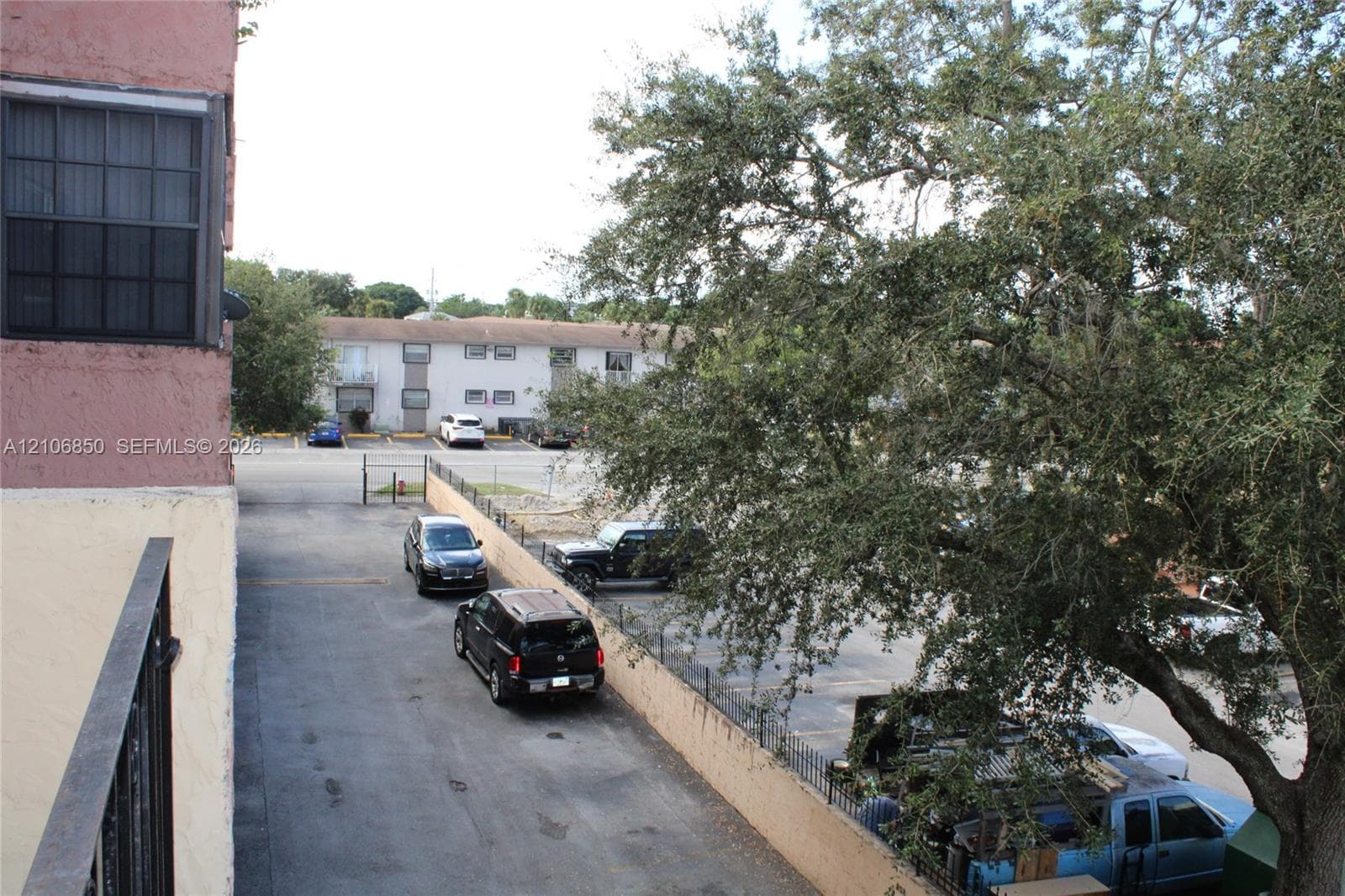 Exterior view featuring metal balcony railing, paved surface parking lot, and mature trees