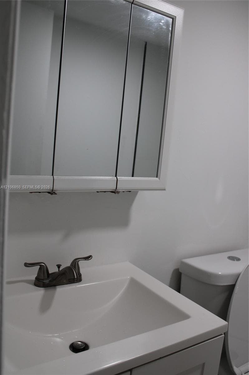 Tri-fold mirrored medicine cabinet, solid-surface vanity countertop with integrated basin, and dual-handle metallic faucet