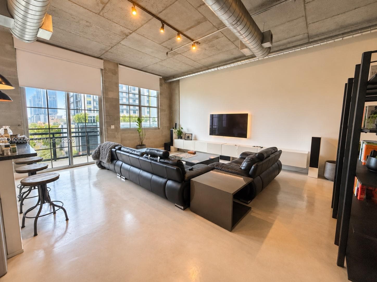 Industrial-style living space featuring exposed concrete ceilings, polished concrete flooring, floor-to-ceiling metal-framed windows, built-in wall-mounted cabinetry, and exposed spiral ductwork