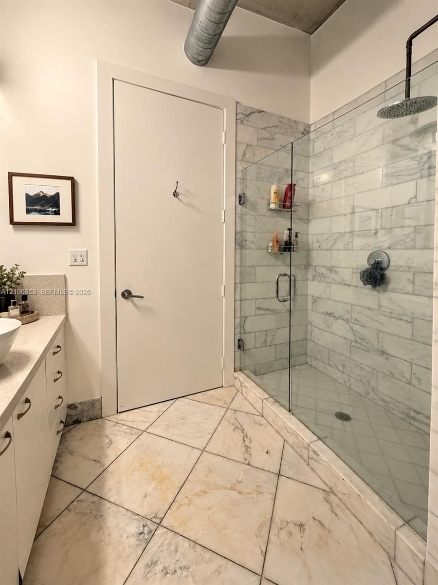 Walk-in shower featuring glass enclosure, subway-tiled surround, and rainfall showerhead, complemented by diagonal-set stone tile flooring and exposed industrial-style ductwork