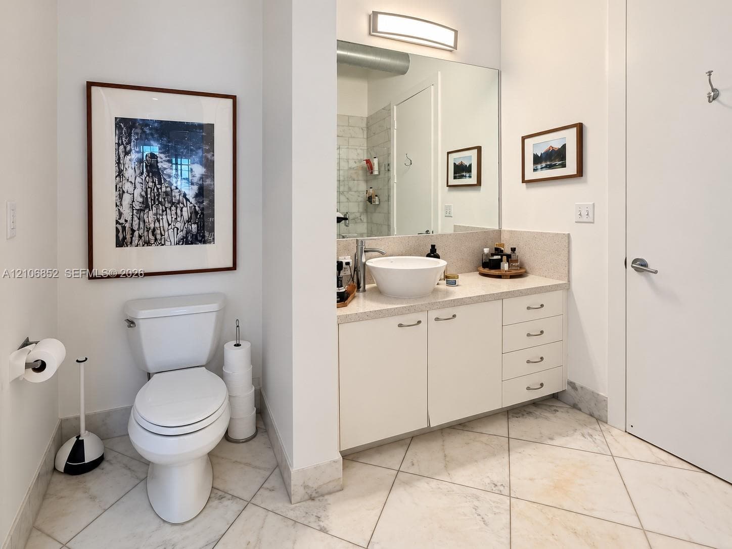 Vanity featuring an integrated cabinet with drawers, solid surface countertop, white vessel sink, and wall-mounted light fixture, paired with stone-finish floor tiling