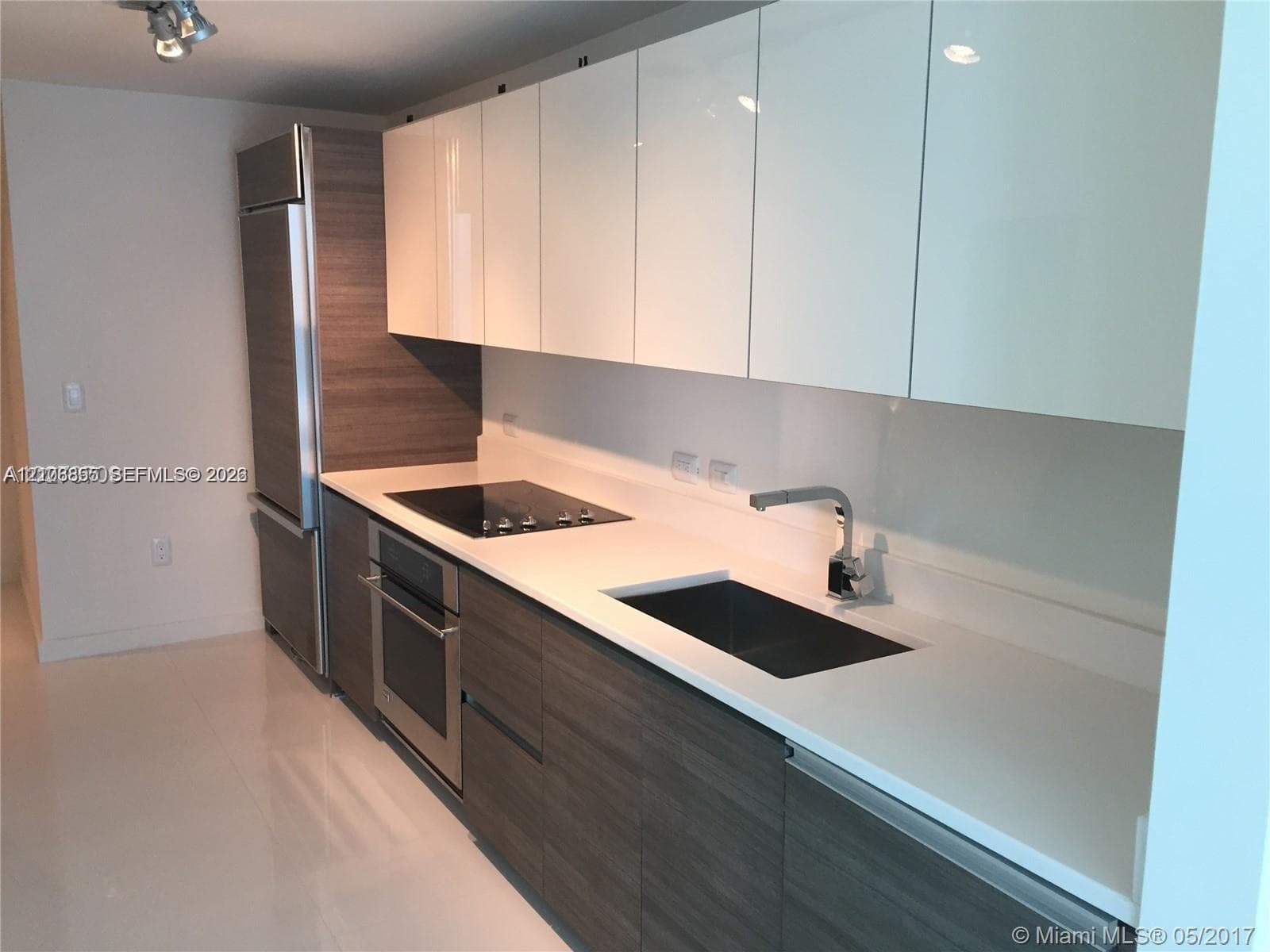 Kitchen featuring high-gloss upper cabinetry, wood-finish lower cabinetry, integrated refrigerator, solid-surface countertops, and stainless steel built-in oven