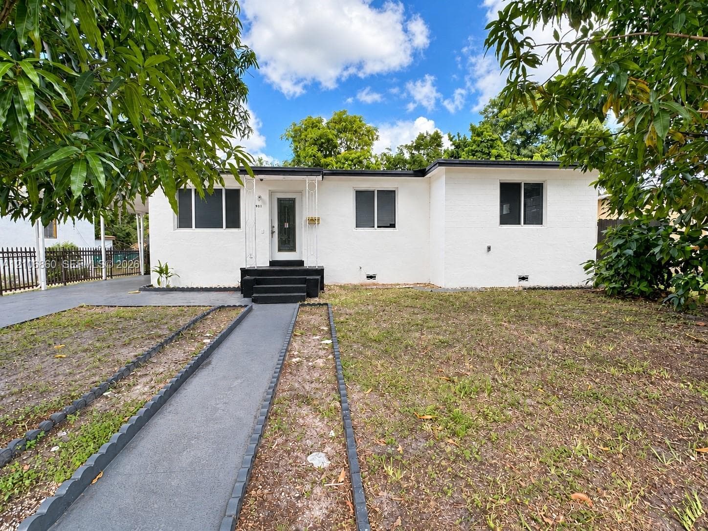Single-story white brick exterior with a dark-finished entry staircase, central glass-paneled door, concrete walkway, and metal perimeter fencing