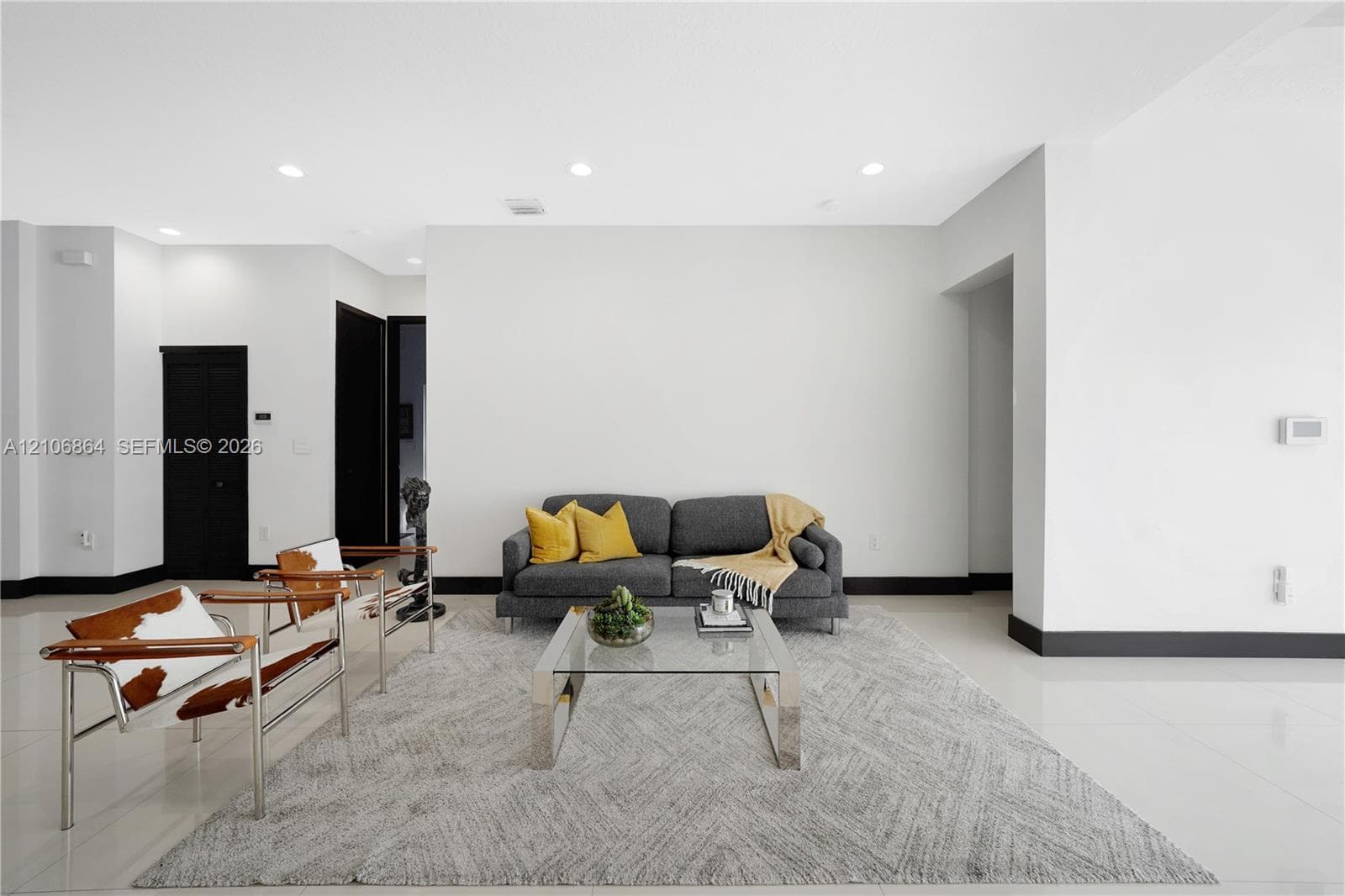 Open-concept living space featuring high ceilings with recessed lighting, large-format tile flooring, a floor-to-ceiling stone-veneer accent wall, and a kitchen equipped with a stainless steel range hood and built-in wine refrigeration