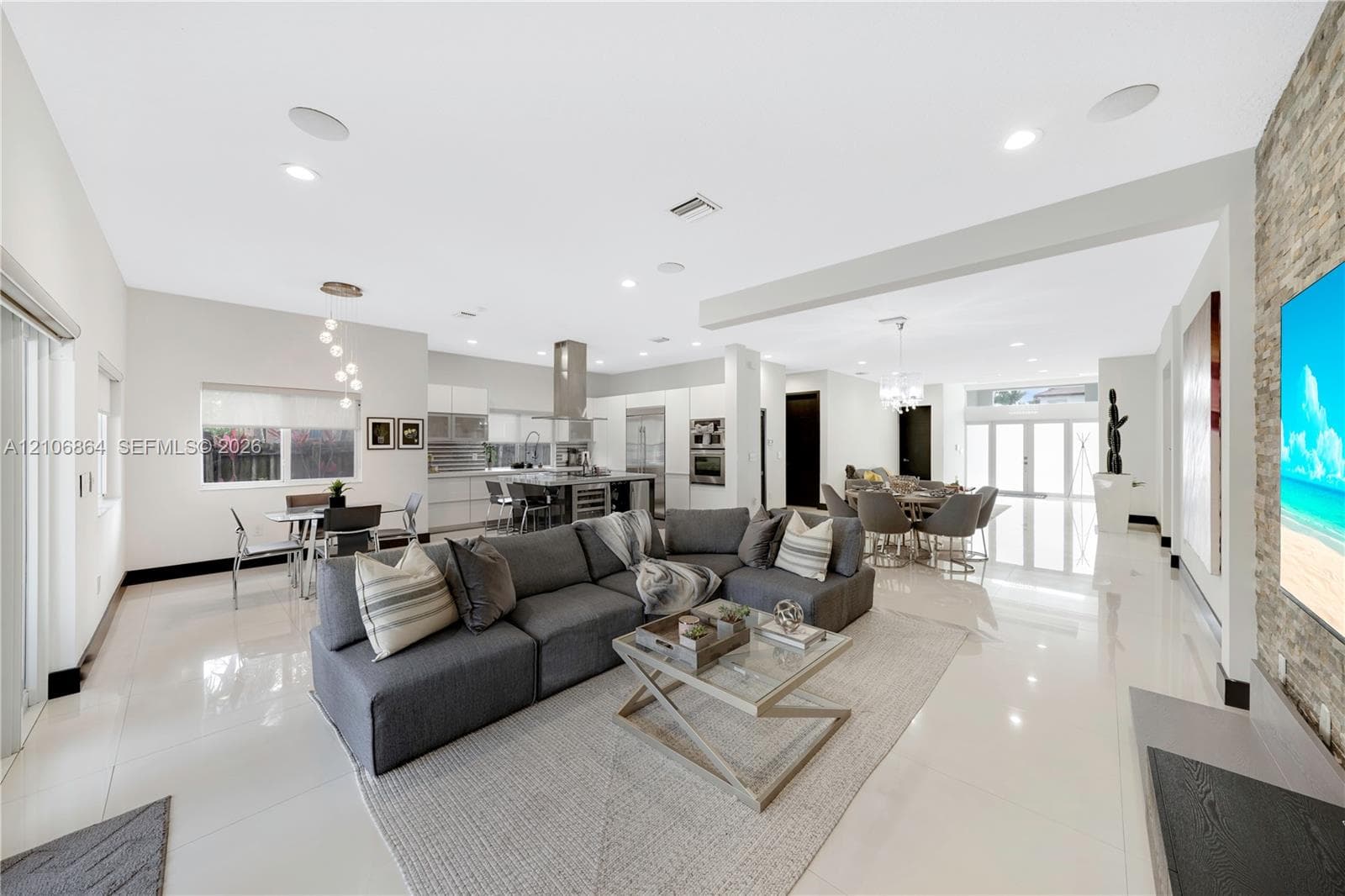 Kitchen featuring high-gloss white cabinetry, a center island with integrated wine refrigeration, stainless steel appliances including a built-in oven and microwave, and large-format tile flooring