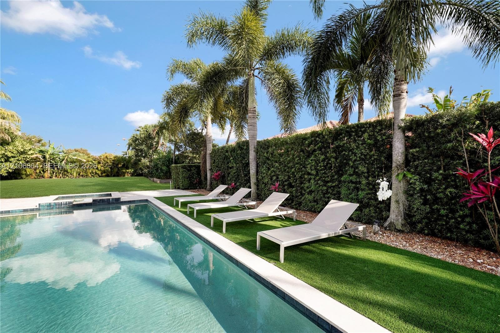 Aerial perspective of a property featuring an in-ground swimming pool, expansive rear lawn, covered patio, and established perimeter landscaping