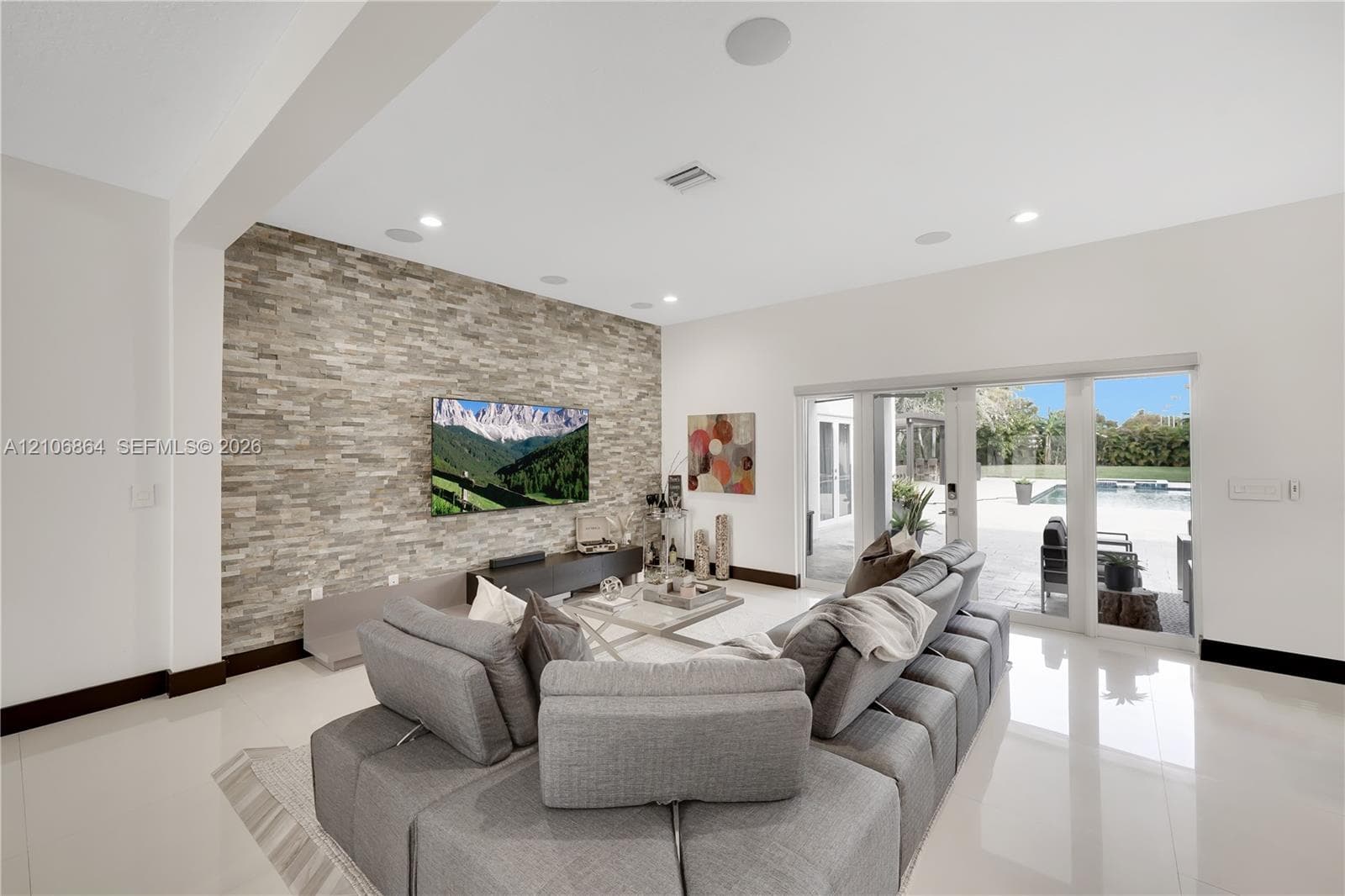 Contemporary kitchen featuring high-gloss cabinetry, a central island with integrated wine storage, a stainless steel chimney-style range hood, polished tile flooring, and built-in stainless steel double ovens
