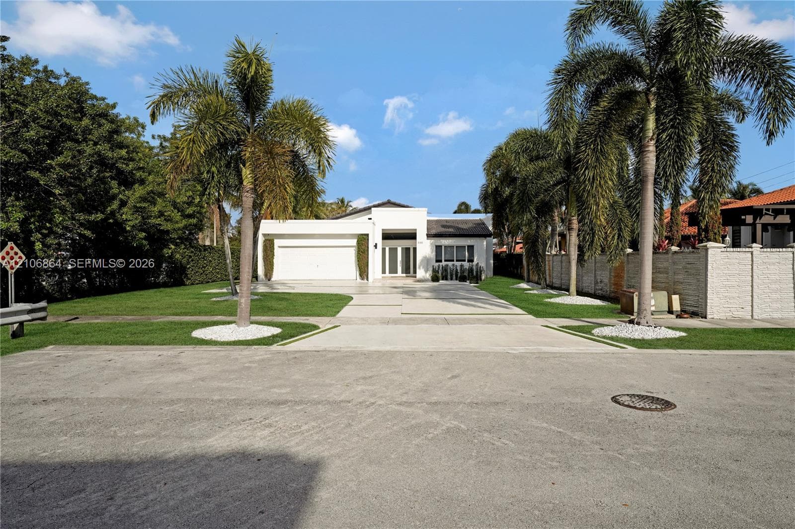Modern single-story exterior featuring a white stucco facade, multi-car garage, concrete paver driveway with integrated landscaping strips, and manicured perimeter lawn