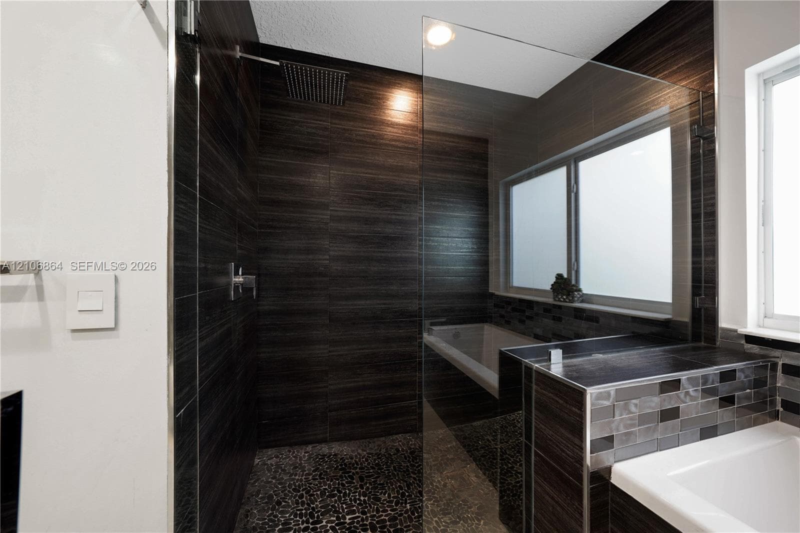 Wall-mounted floating vanity with integrated rectangular sink and wood-finish cabinetry, accented by floor-to-ceiling large-format wall tiling and a decorative glass mosaic tile border