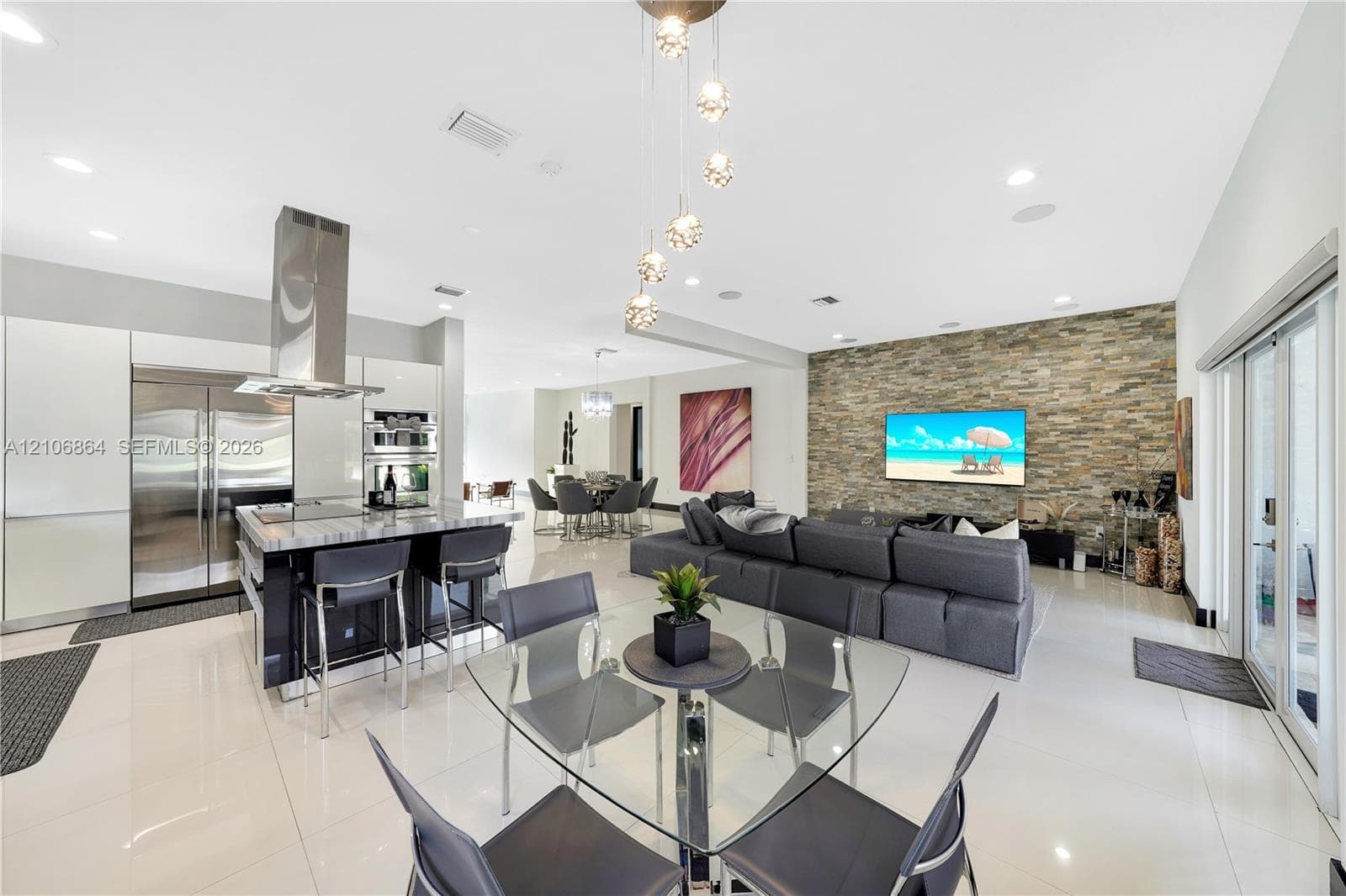 Modern kitchen featuring sleek flat-panel cabinetry, a central island with stone-finish countertops, stainless steel appliances, a chimney-style range hood, and polished flooring
