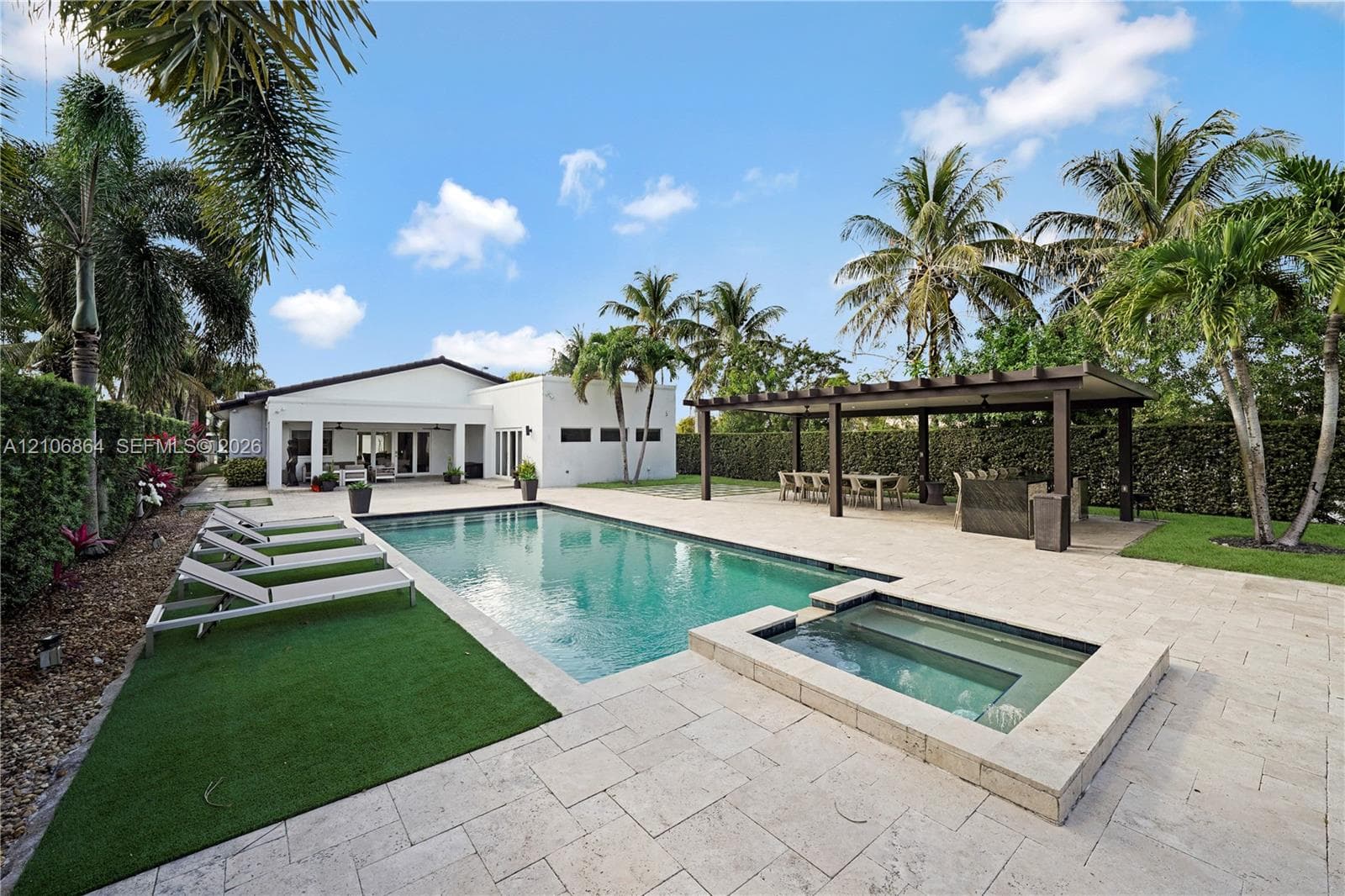 Expansive rear grounds featuring a manicured lawn, established perimeter hedges, and mature palm trees