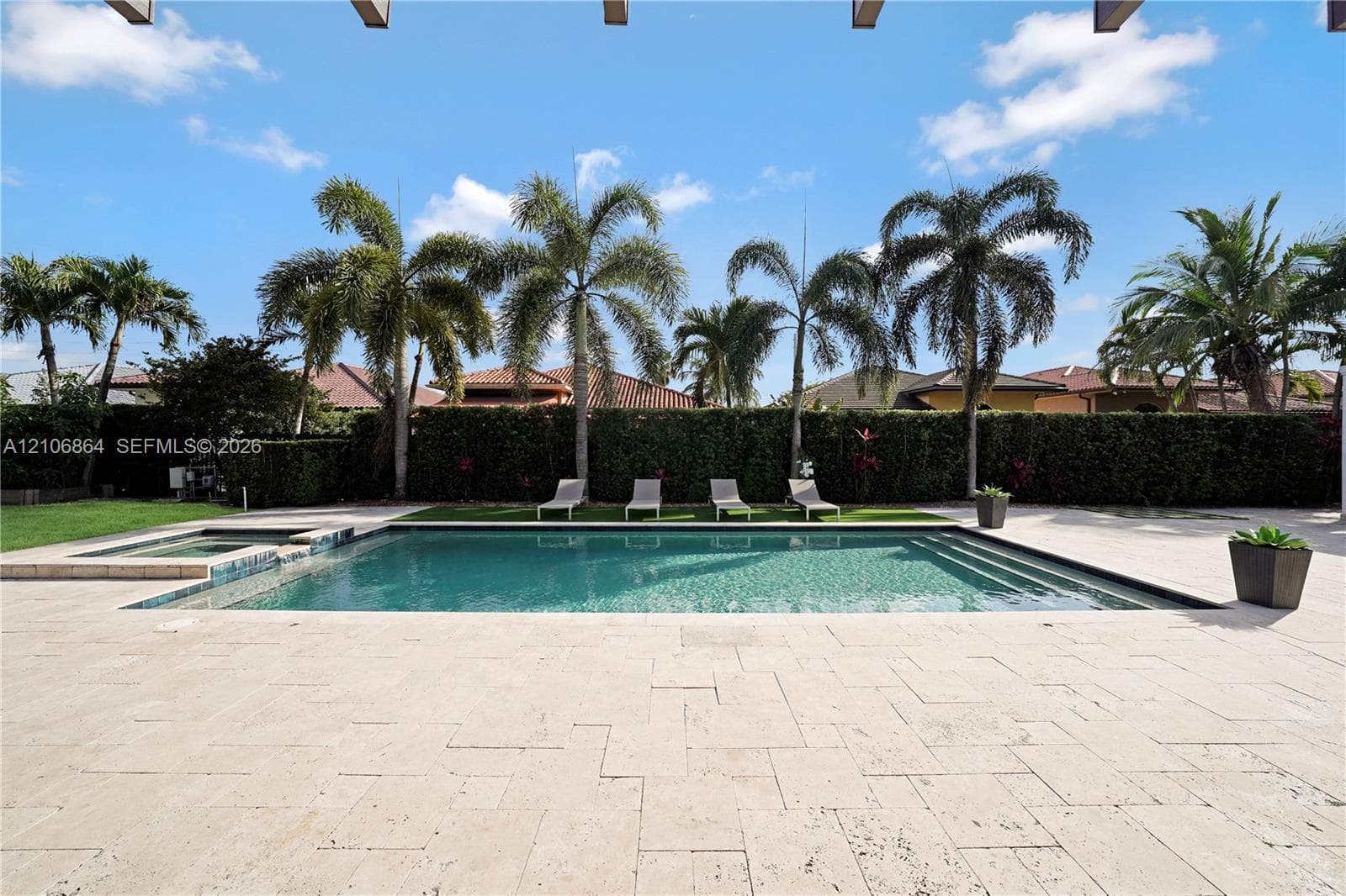 Aerial perspective of a sprawling parcel featuring a rectangular swimming pool, extensive paved patio, manicured lawn, and perimeter landscaping