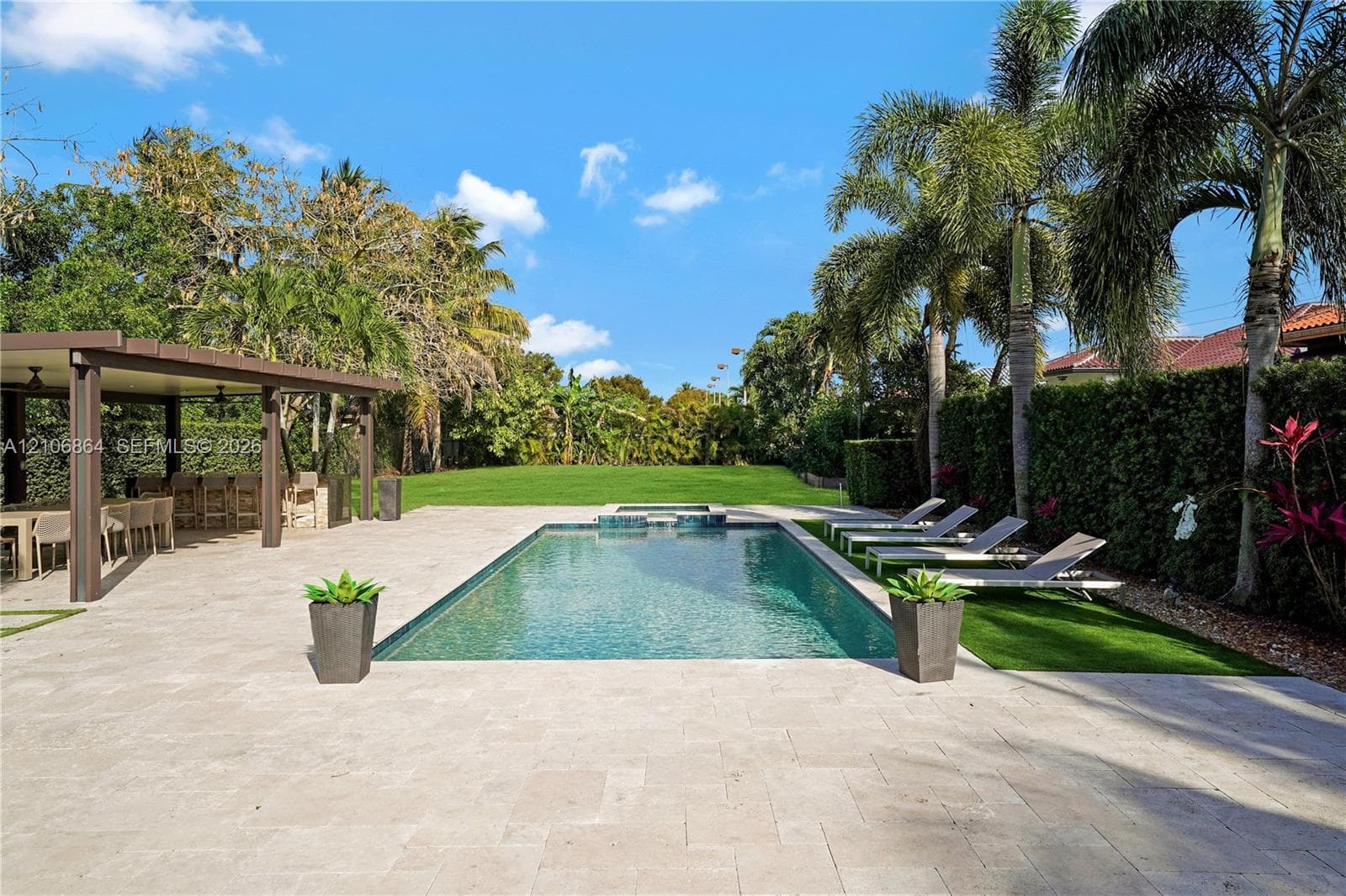 Aerial perspective featuring a residential property with a paved driveway, manicured lawn, mature palm trees, and an in-ground swimming pool