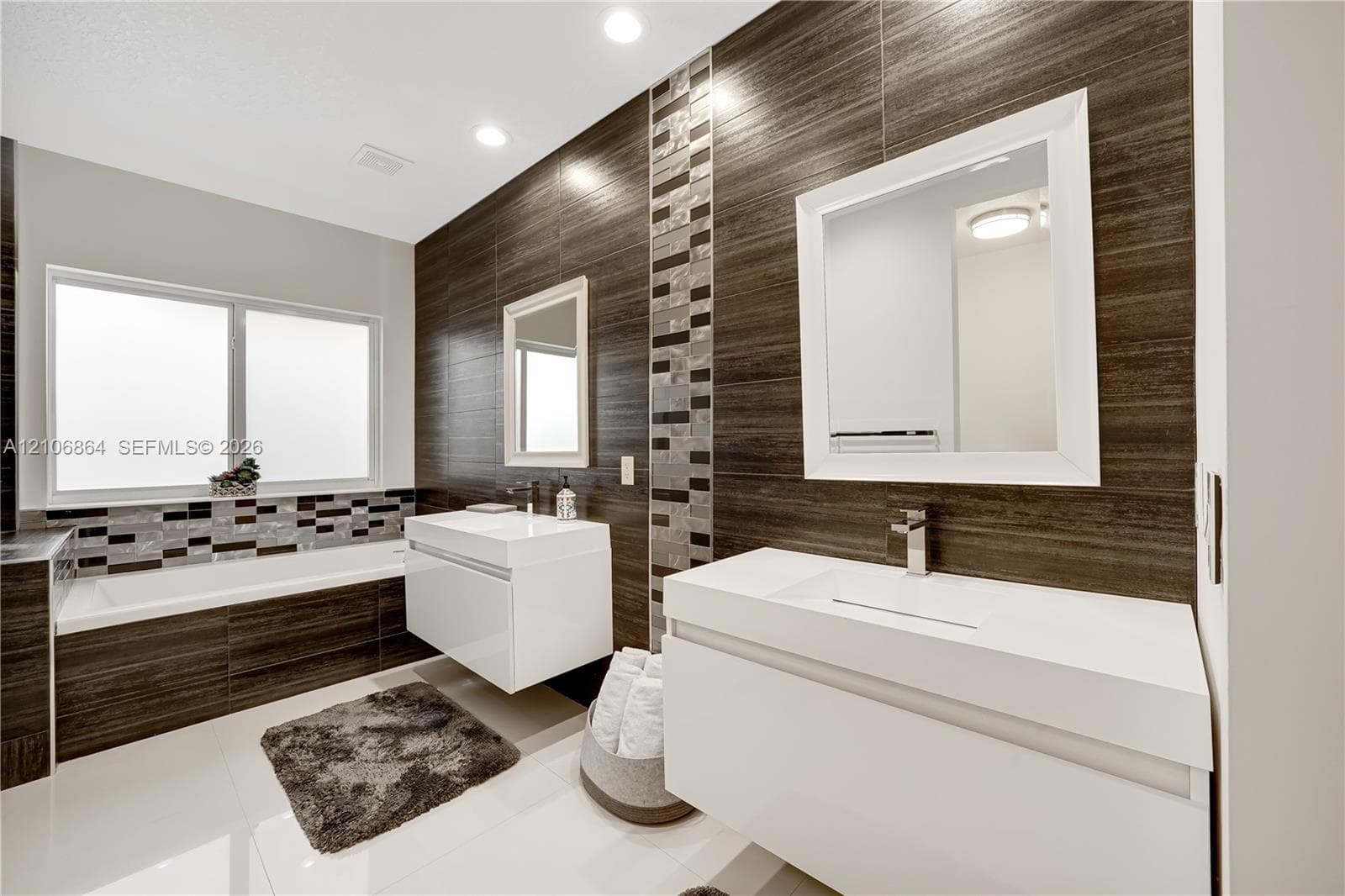 Walk-in shower with dark horizontal wall tile, pebble-texture floor, rain-style shower head, frameless glass enclosure, and a built-in soaking tub with mosaic tile surround