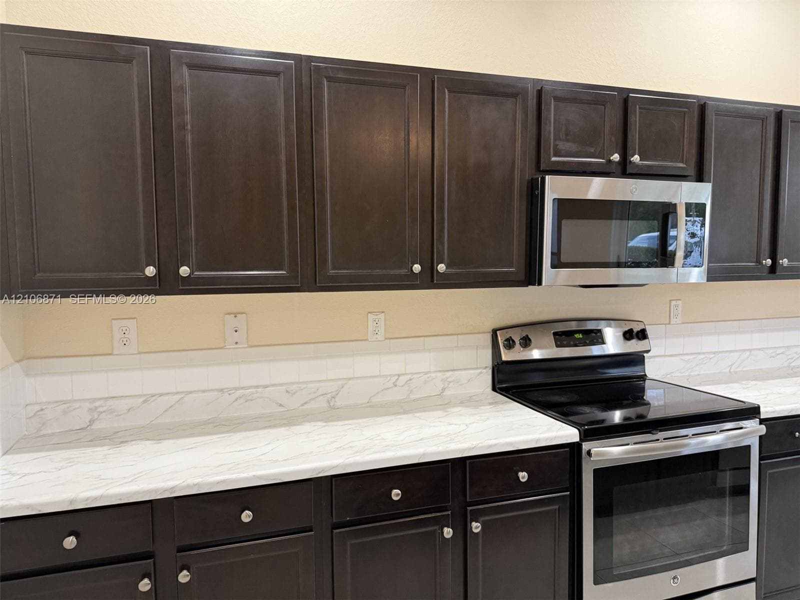 Dark-toned cabinetry featuring shaker-style doors, light-veined countertops, white subway tile backsplash, and stainless steel appliances