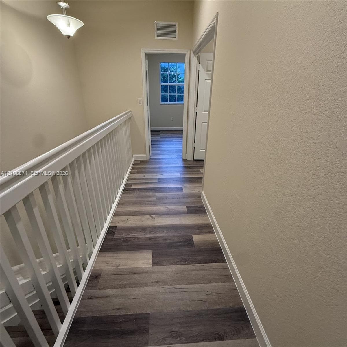 Hallway featuring wood-finish flooring, white spindle railings, and a pendant light fixture