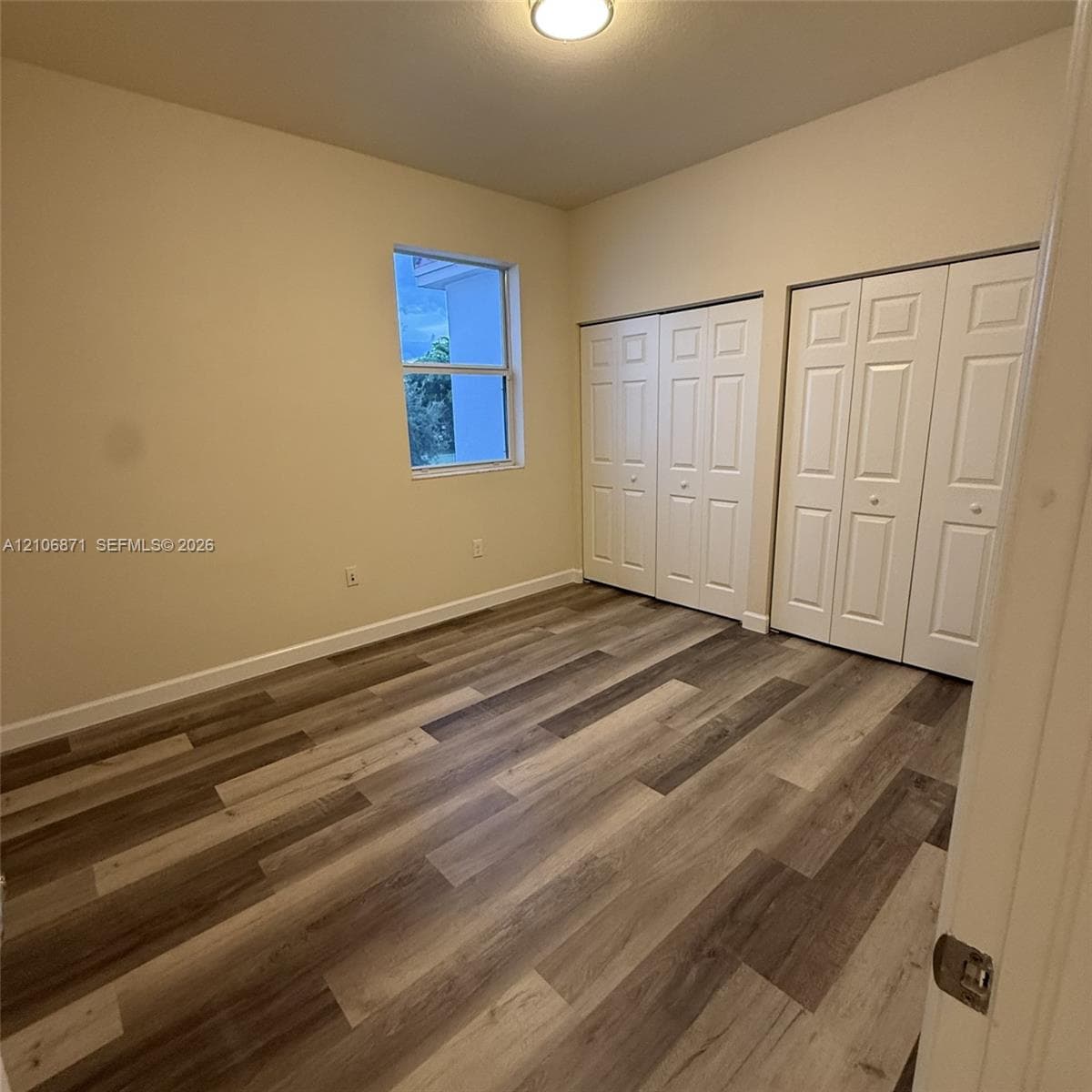 Room featuring wood-finish flooring, dual bi-fold door closets, a single-pane window, and a flush-mount ceiling light fixture