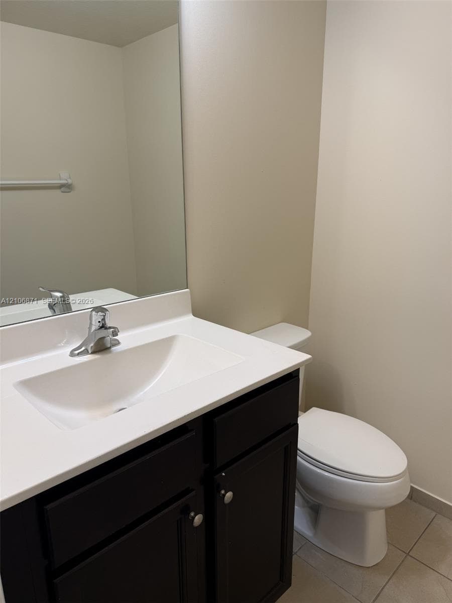 Vanity featuring a dark-finish cabinet, solid-surface countertop, integrated rectangular sink, chrome-finish faucet, and a wall-mounted mirror