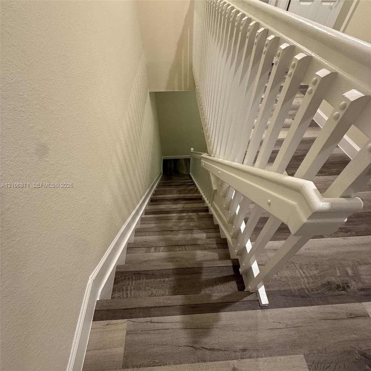 Staircase featuring wood-finish flooring, white wooden balusters, and a matching handrail